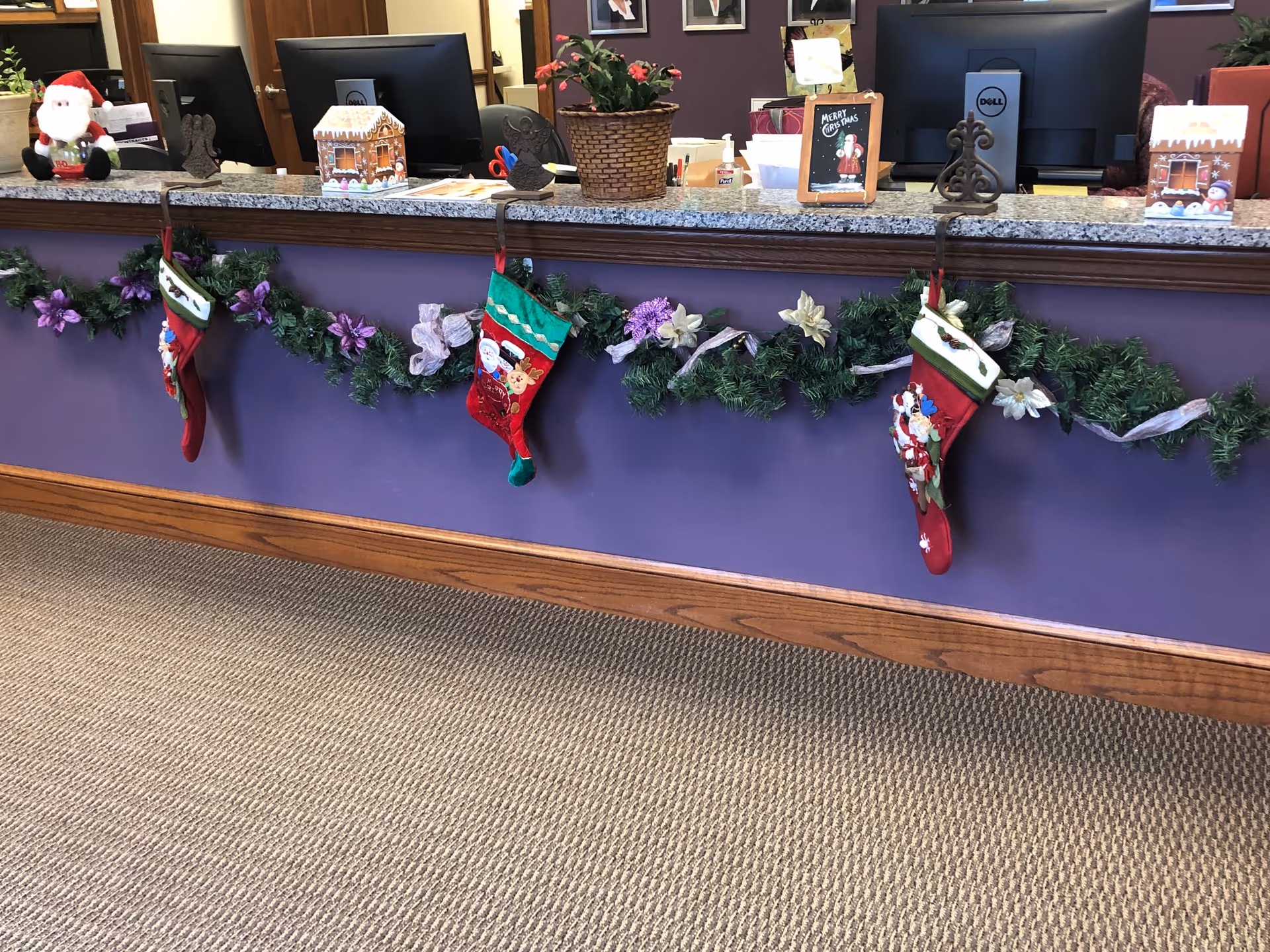 Reception counter decorated with Christmas garlands, stockings, and festive decor inside a purple-walled lobby.