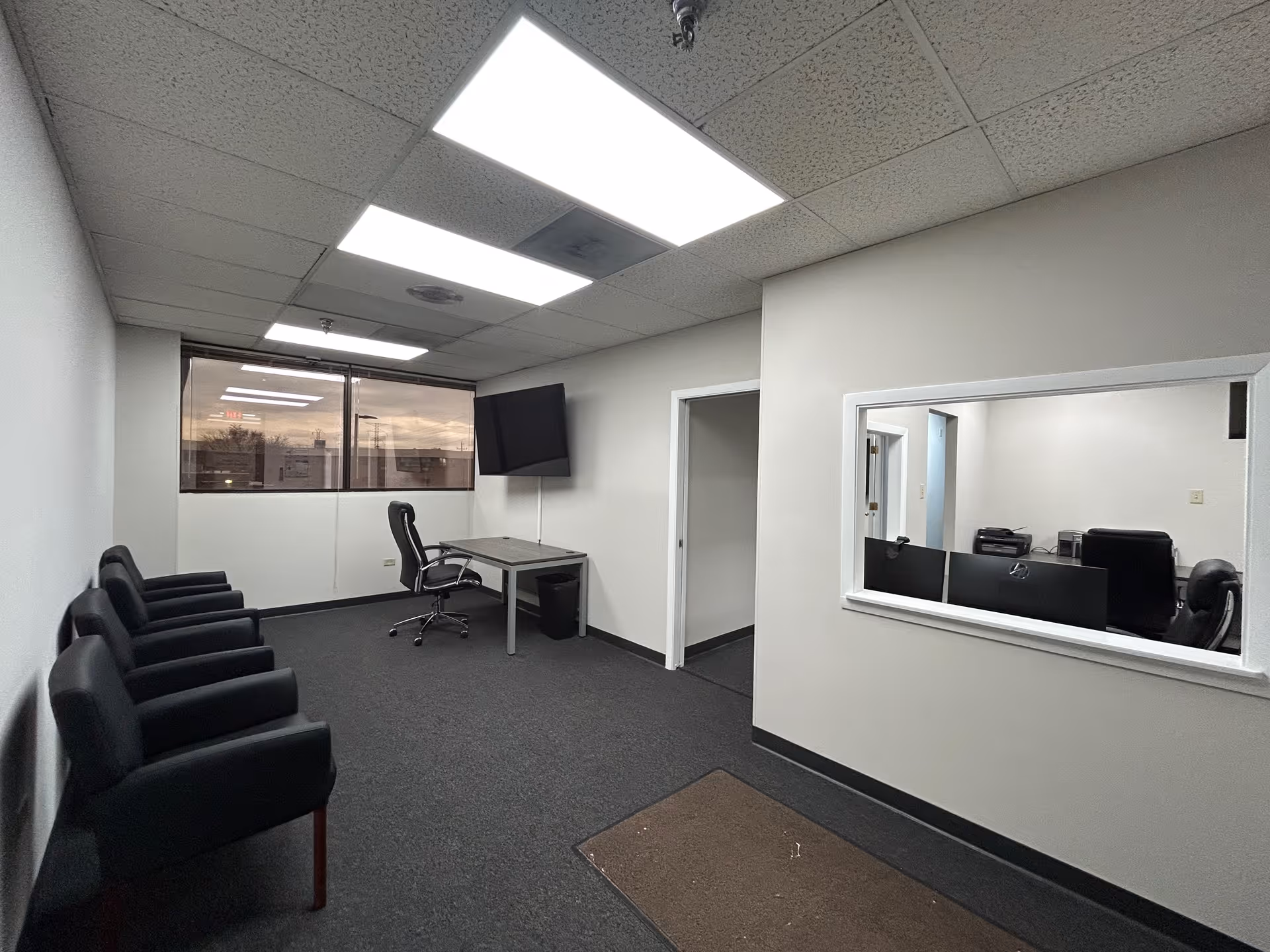 An empty facility office area with a desk, several chairs along the wall, and a window.