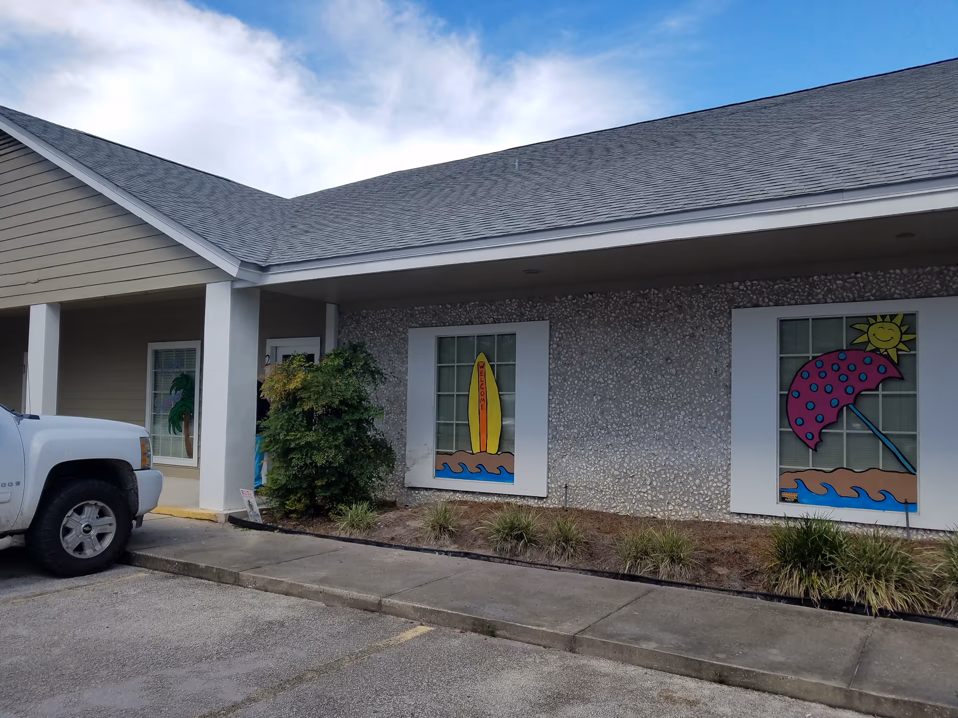 Exterior view of Welcome Homecare facility with beige walls, window art, and a parked truck.