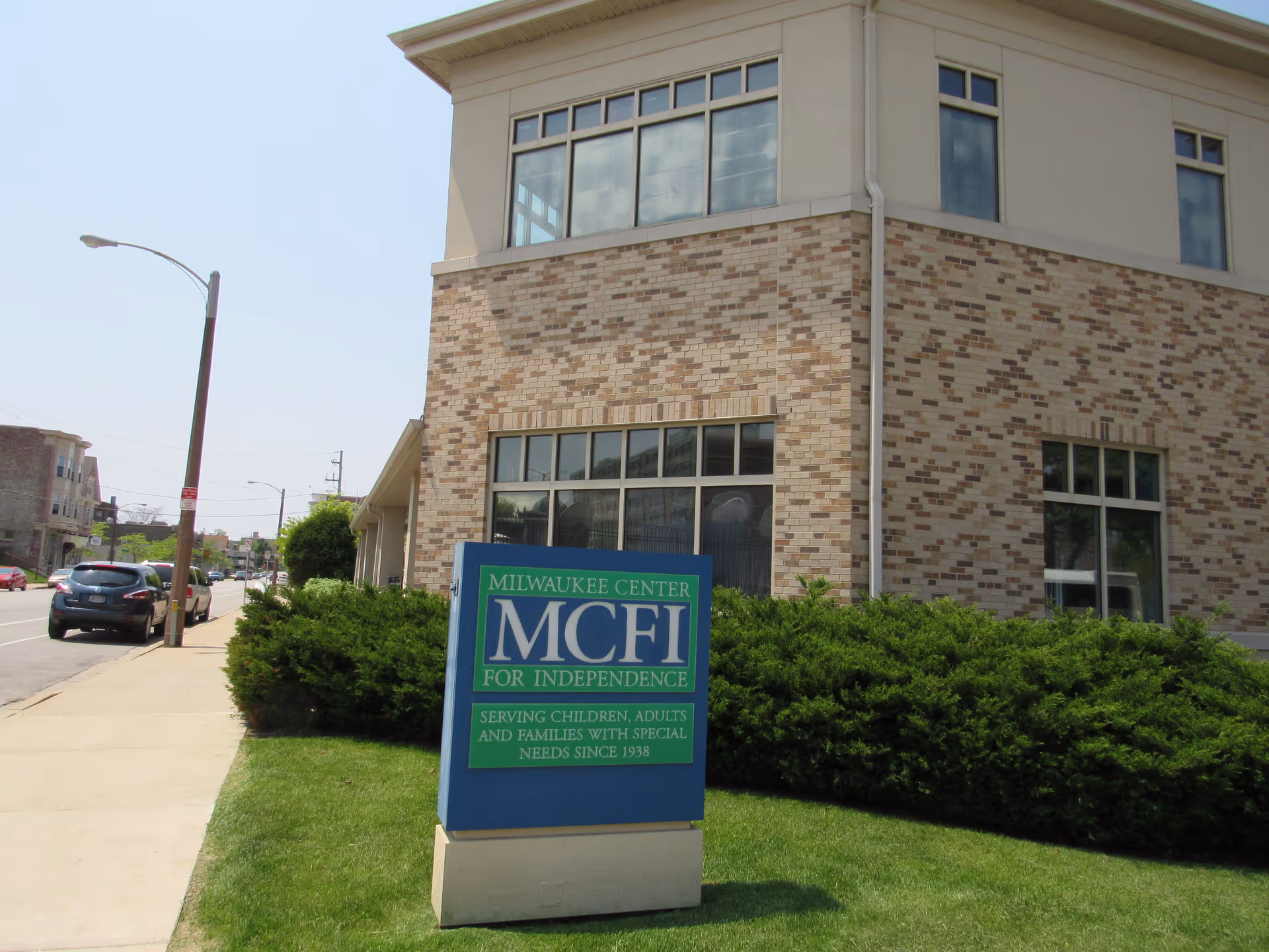 Exterior view of a brick building with a blue MCFI sign in front landscaping.