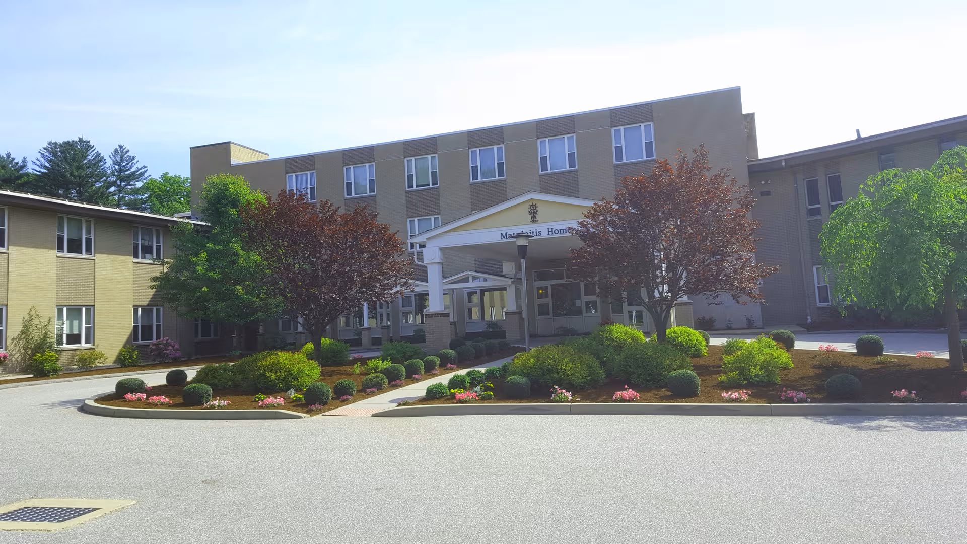 Exterior view of Matulaitis Nursing Home showing the entrance, sidewalks, and landscaped shrubs.