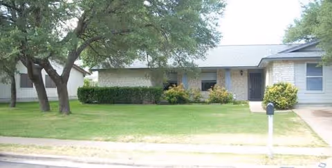 Single-story senior living facility with a green lawn, trees, shrubs, and a driveway in front.