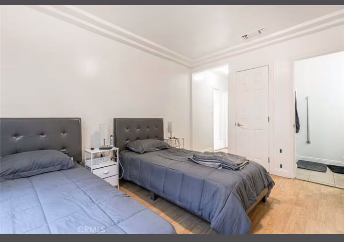 Two twin beds with gray bedding and matching headboards in a bright bedroom.