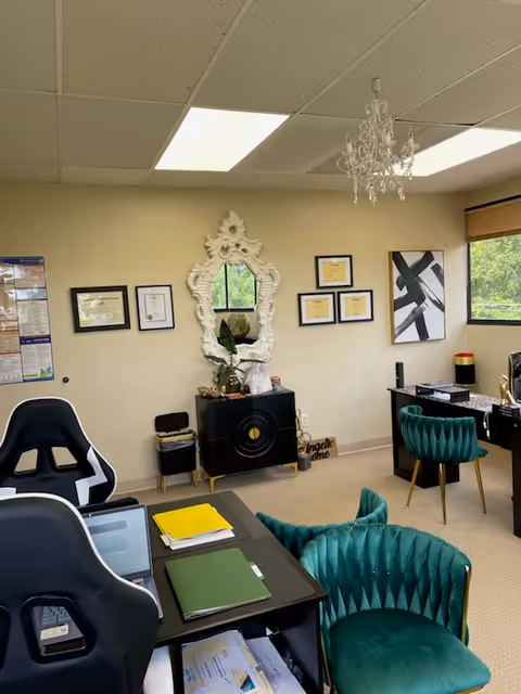 Reception area with green velvet chairs, chandelier, ornate mirror, framed certificates, and desks.