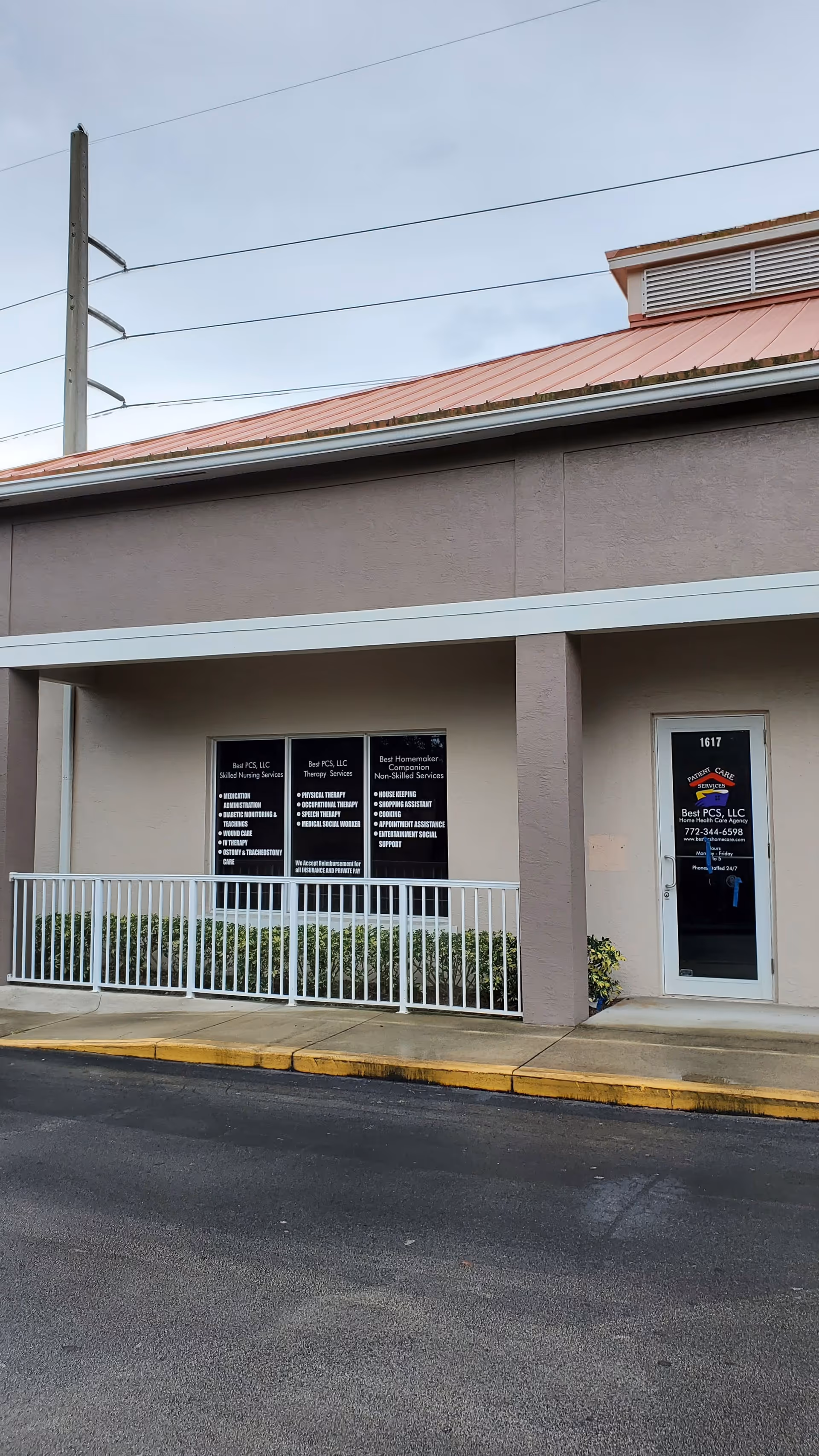 Exterior of a beige building with a red roof, white railing, and signage on windows.