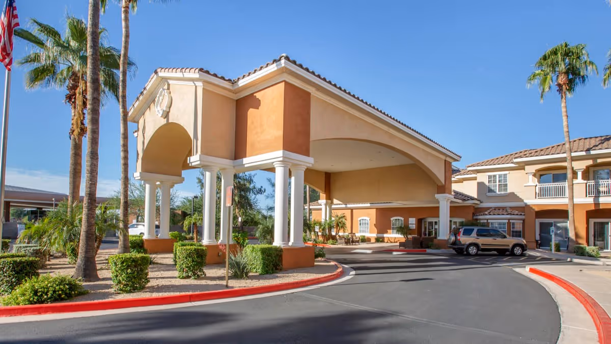 Exterior entrance to a senior living facility with arches, pillars, and palm trees.