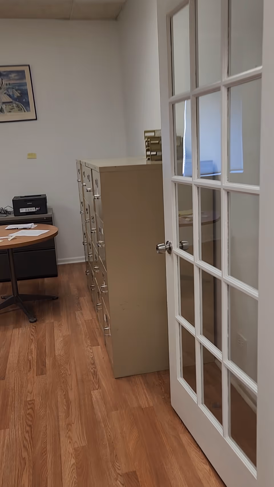 A narrow office area with filing cabinets, a desk, and glass-paneled doors.