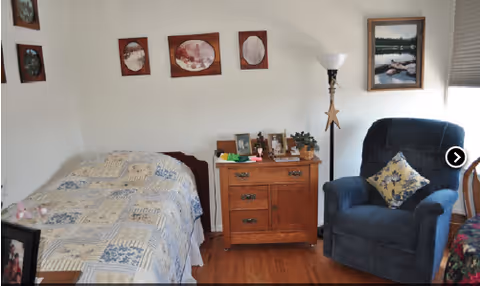 A bedroom in a senior living facility with a bed, dresser, and blue chair.