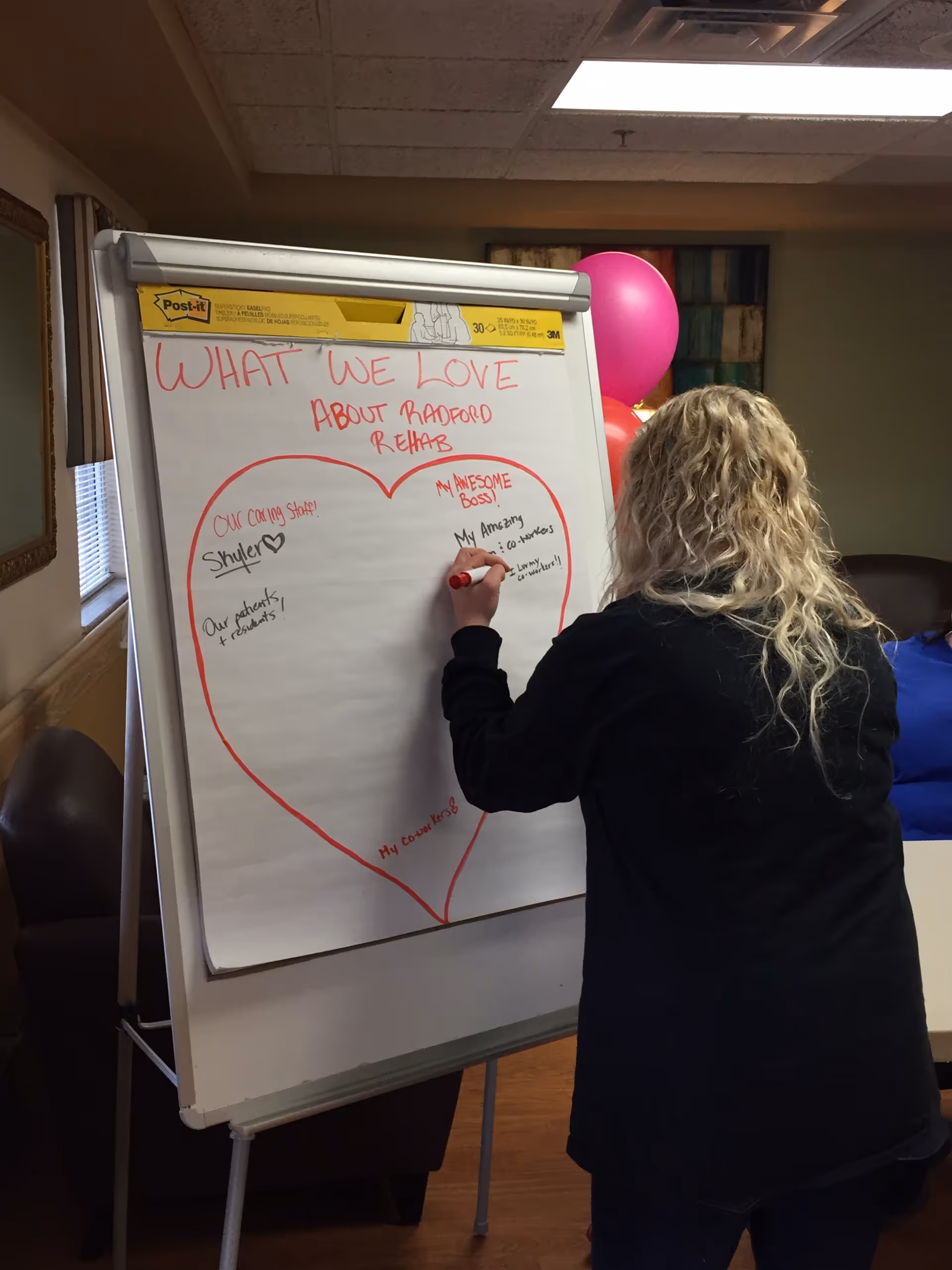 A person writes on a large heart-shaped diagram on a whiteboard indoors.