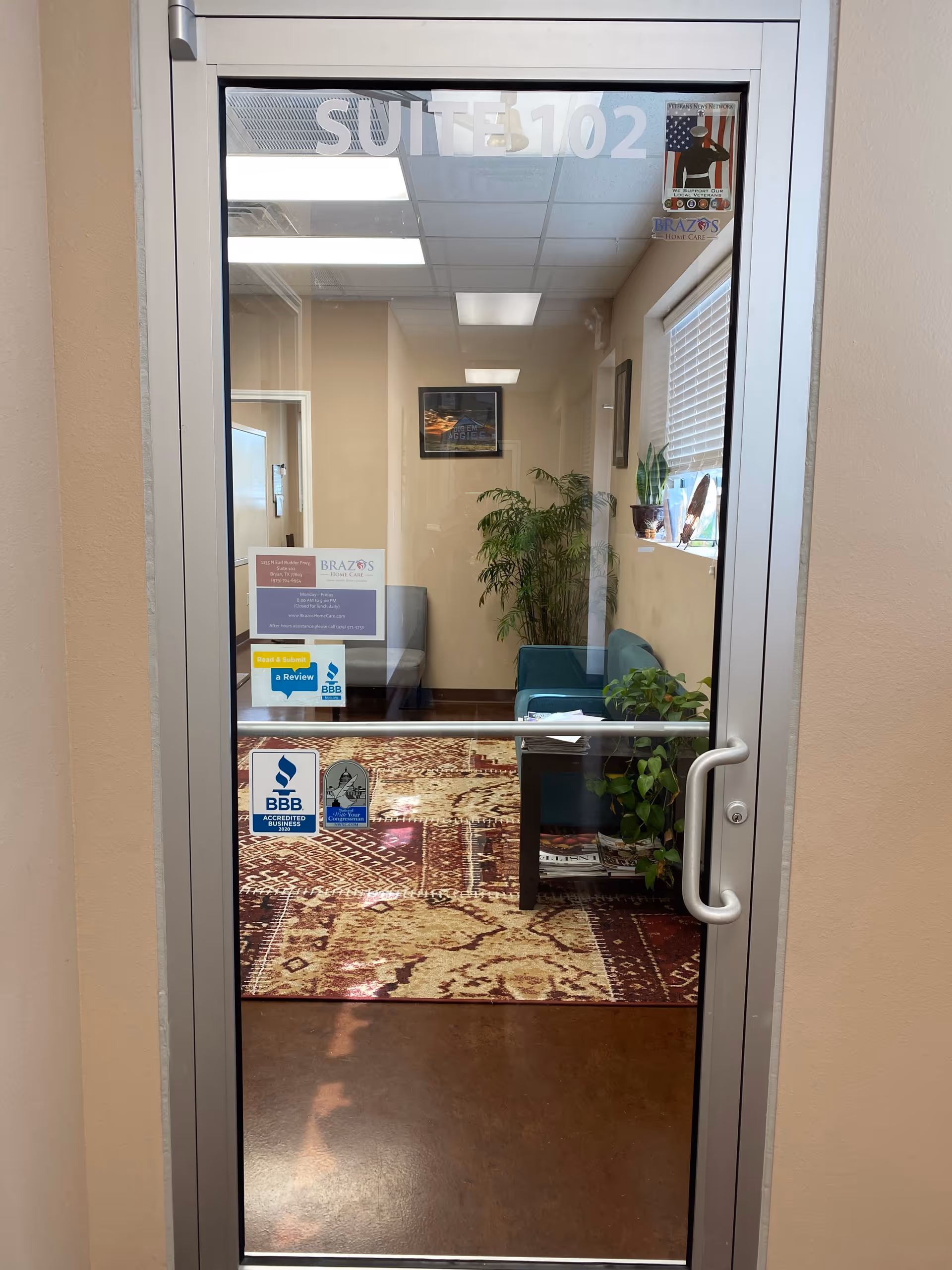Through a glass door, a small lobby with seating, plants, and framed art is visible.