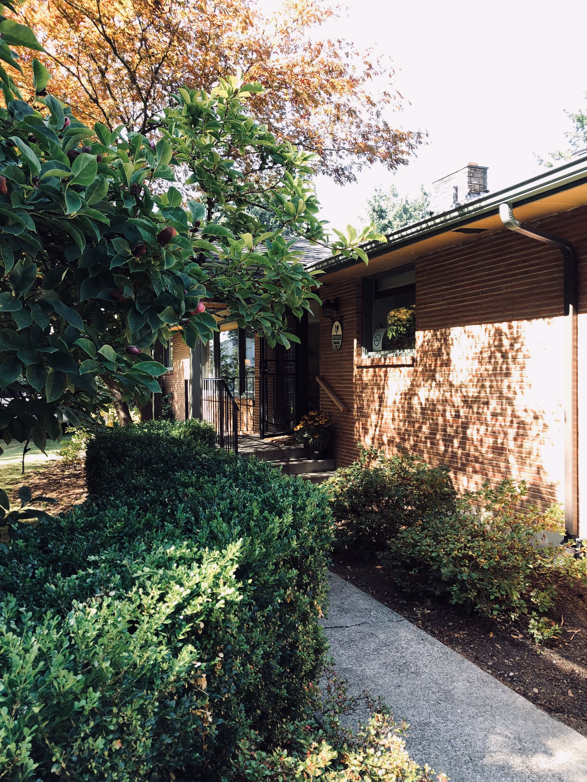 Exterior of a brick care home with a walkway and lush shrubs.