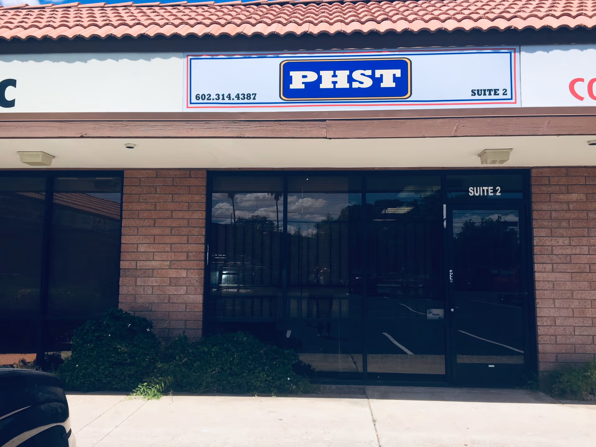 Brick storefront with glass doors labeled Suite 2 and a PHST sign above.