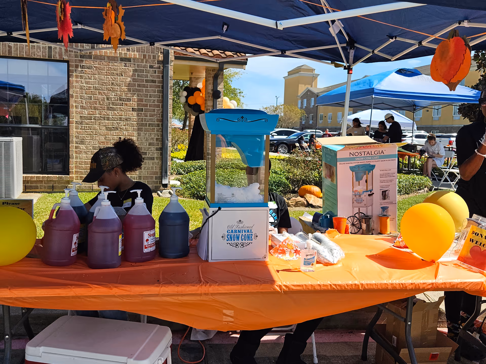 Outdoor event at a senior facility with a serving table, syrup bottles, and snow cone machine.