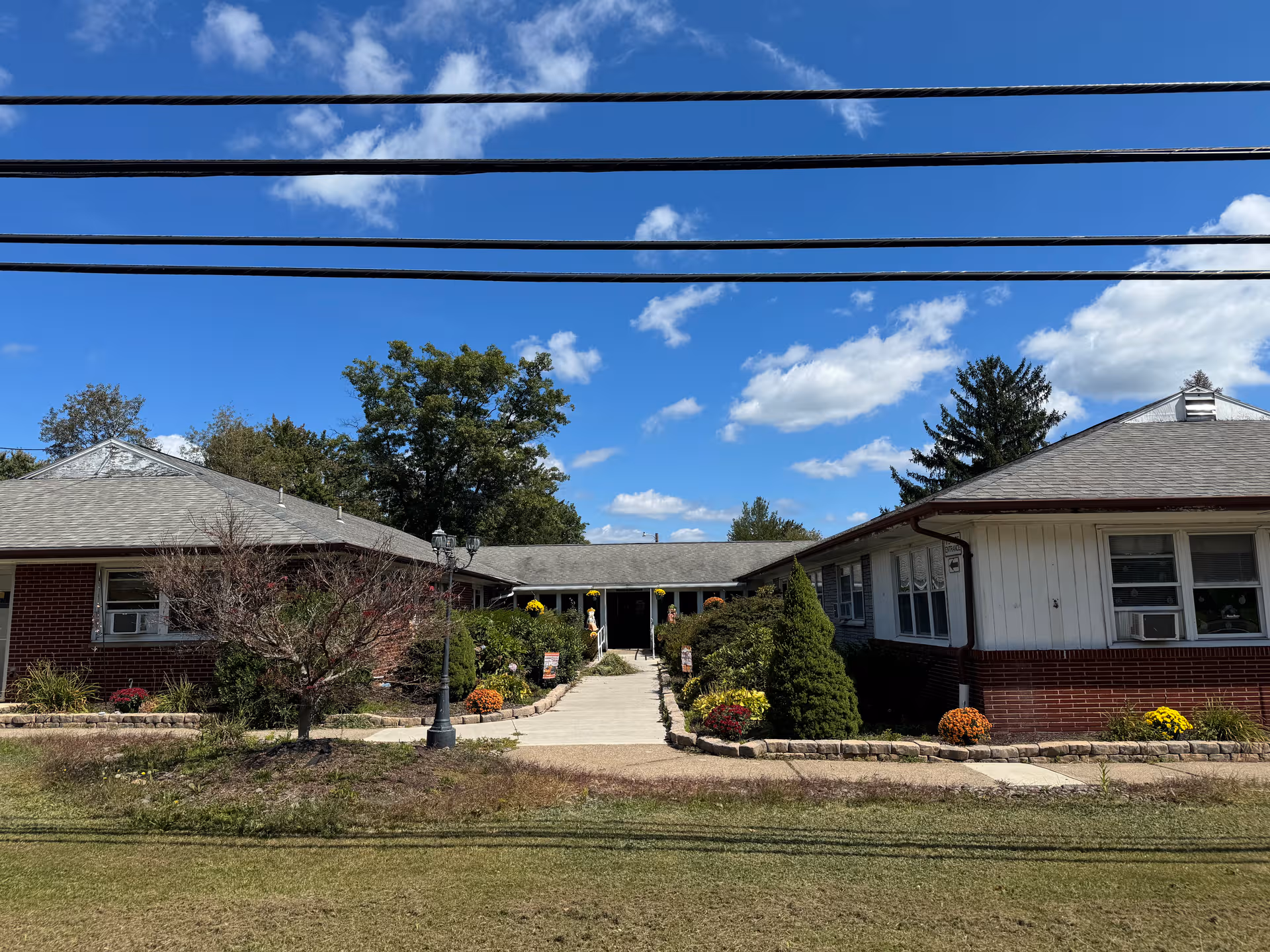 Single-story senior living facility with a central entrance, walkway, and landscaped front yard under blue sky.