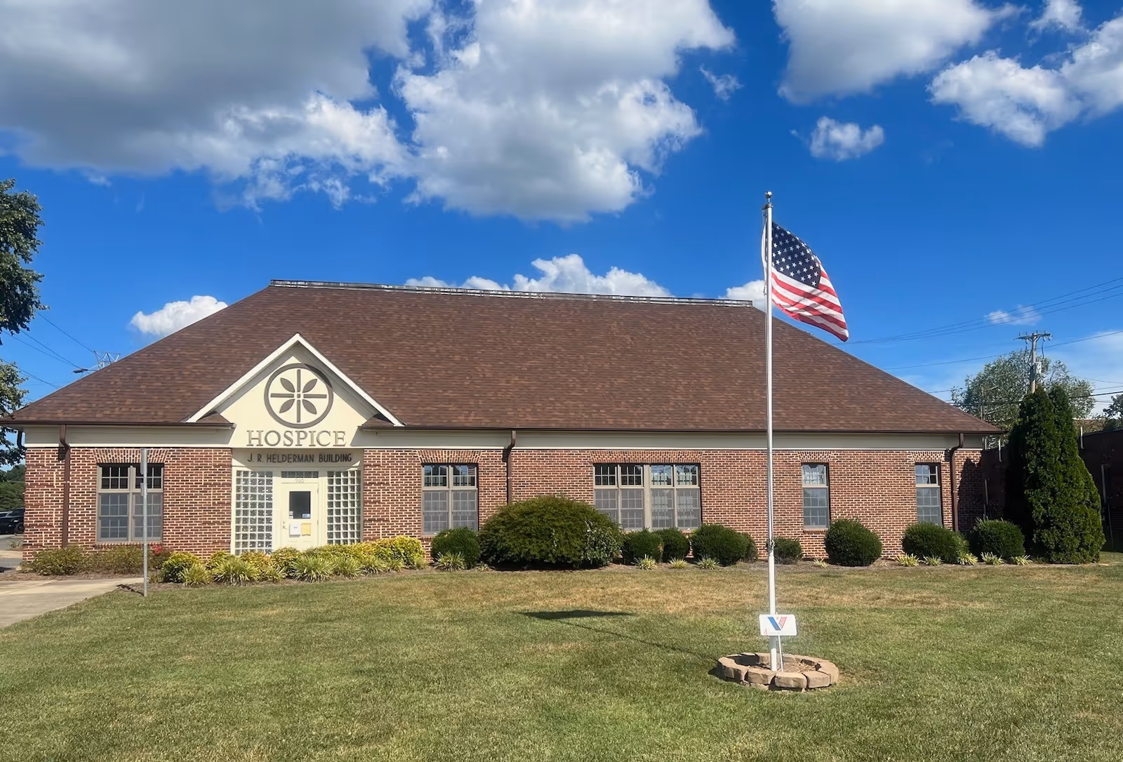 Front view of a brick hospice building with flagpole and landscaped lawn.