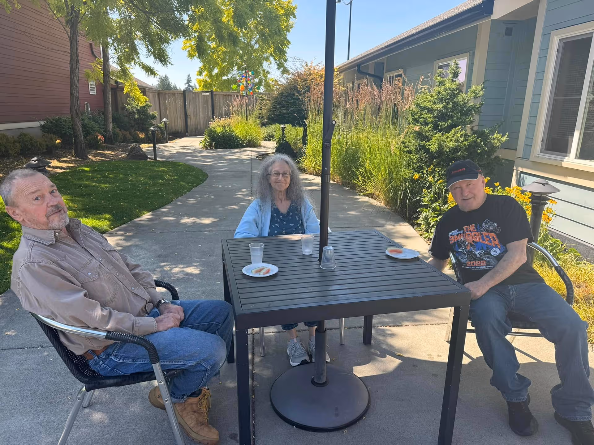 Three seniors sit at a black outdoor table in the Cottages of Edgewood courtyard.