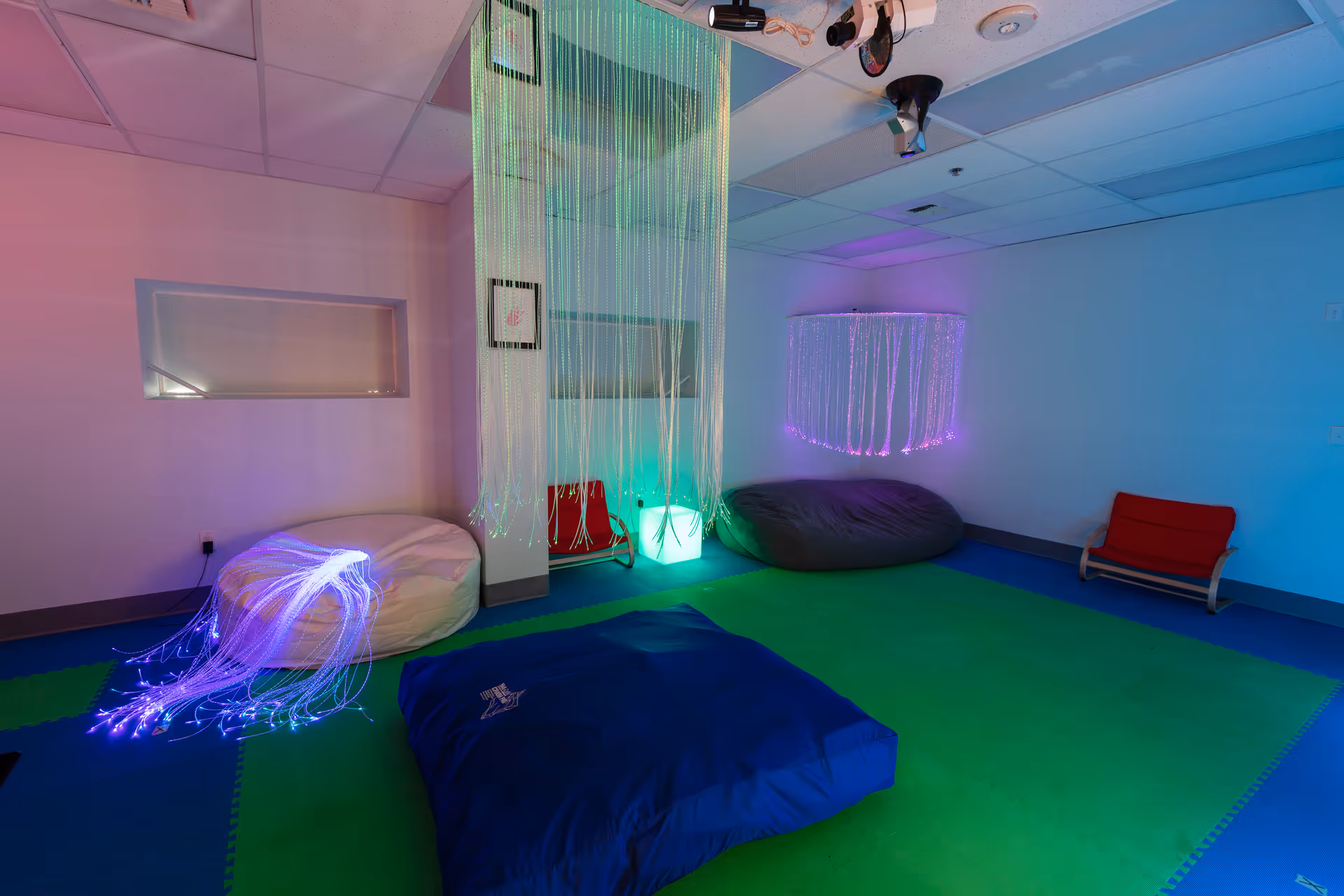 Colorful sensory play room with hanging strands and soft cushions in a calm interior.