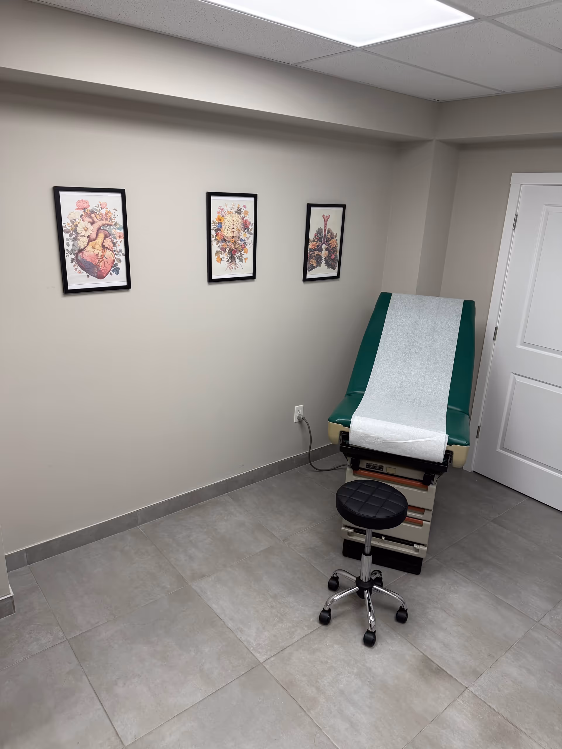 Small medical exam room with green chair, paper sheet, and rolling stool.