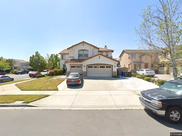 Two-story suburban house with a three-car garage and cars parked in the driveway on a sunny day.