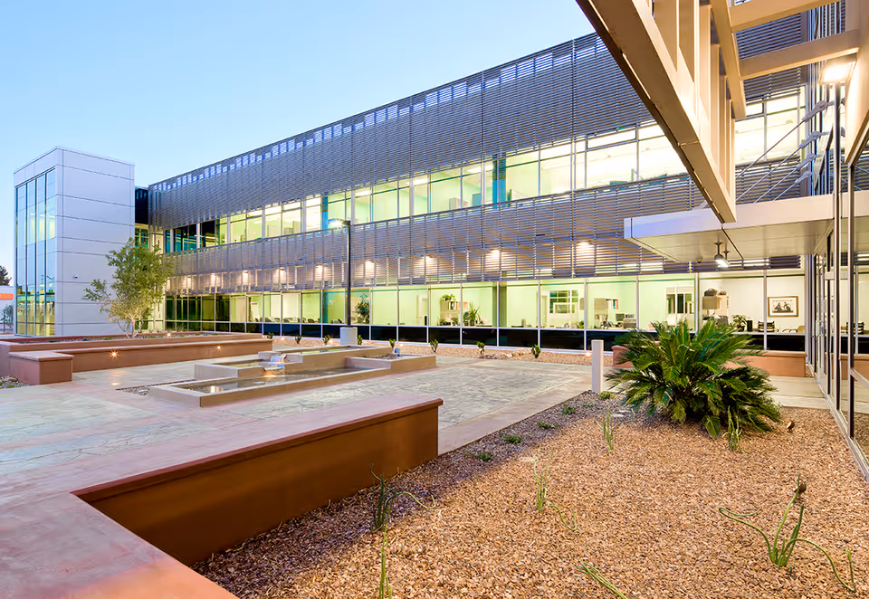 Modern facility exterior with glass walls and a landscaped outdoor courtyard featuring a water fountain.