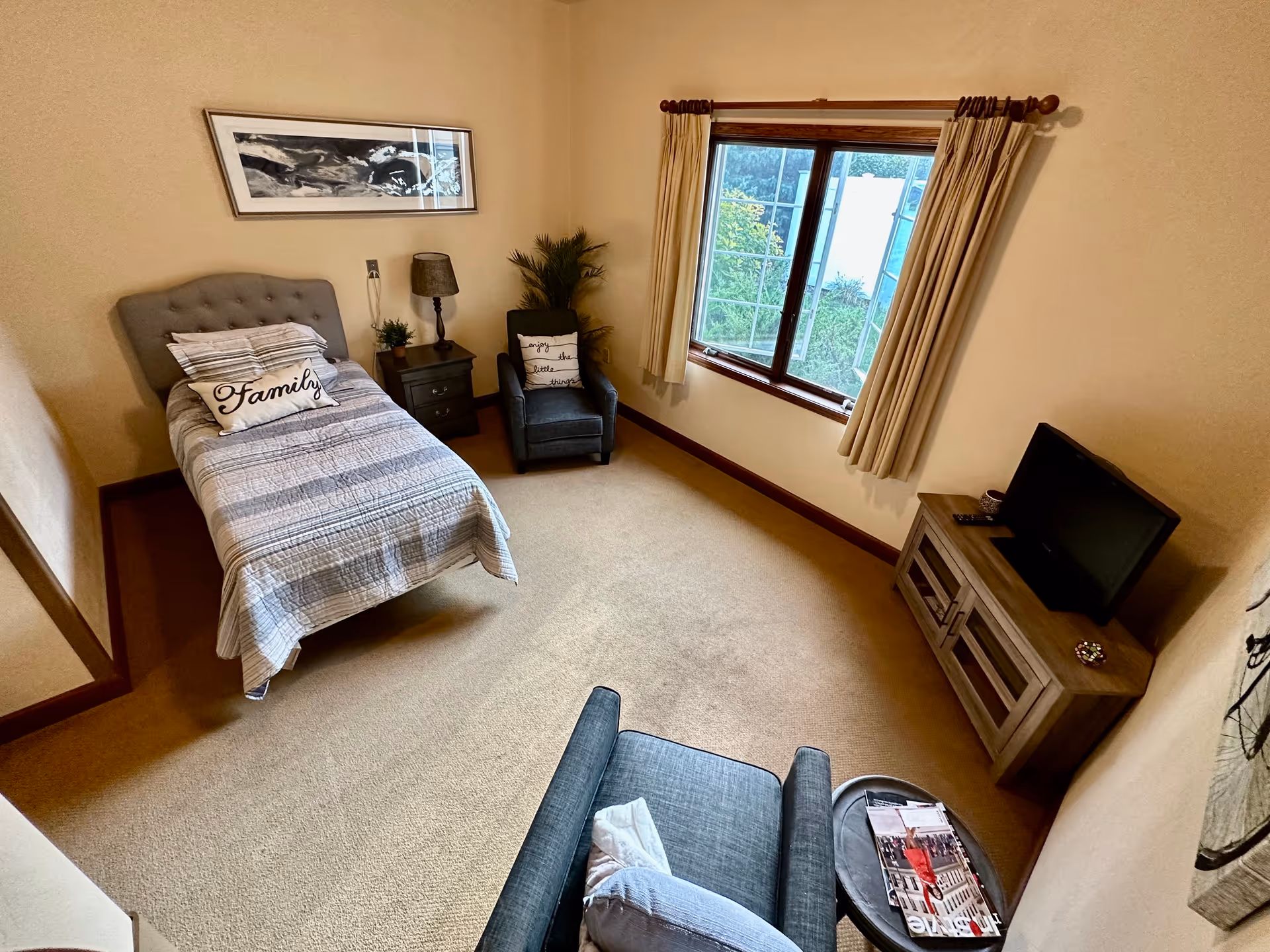 A cozy bedroom in a senior living unit with a bed, seating, and a TV.