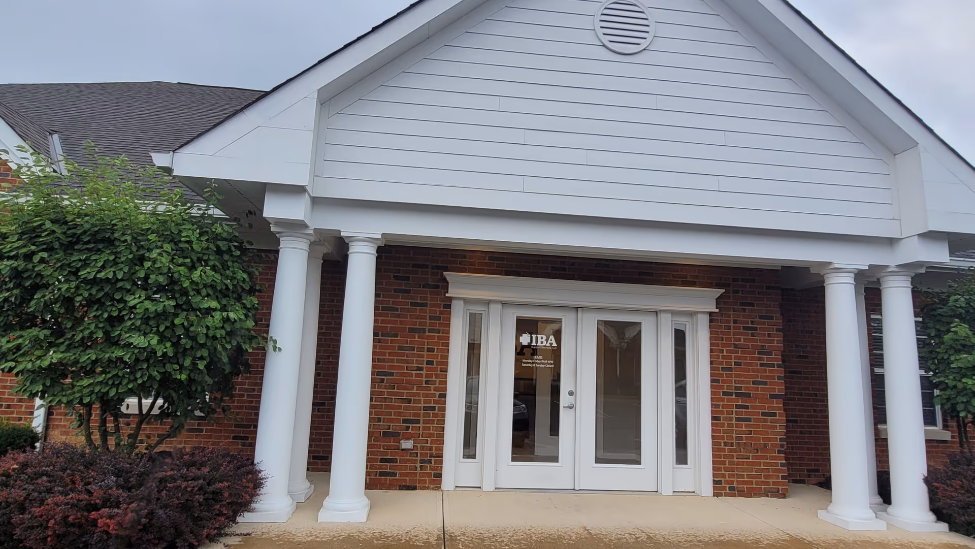 A brick senior living facility entrance with white columns and double doors labeled IBA Support Services.