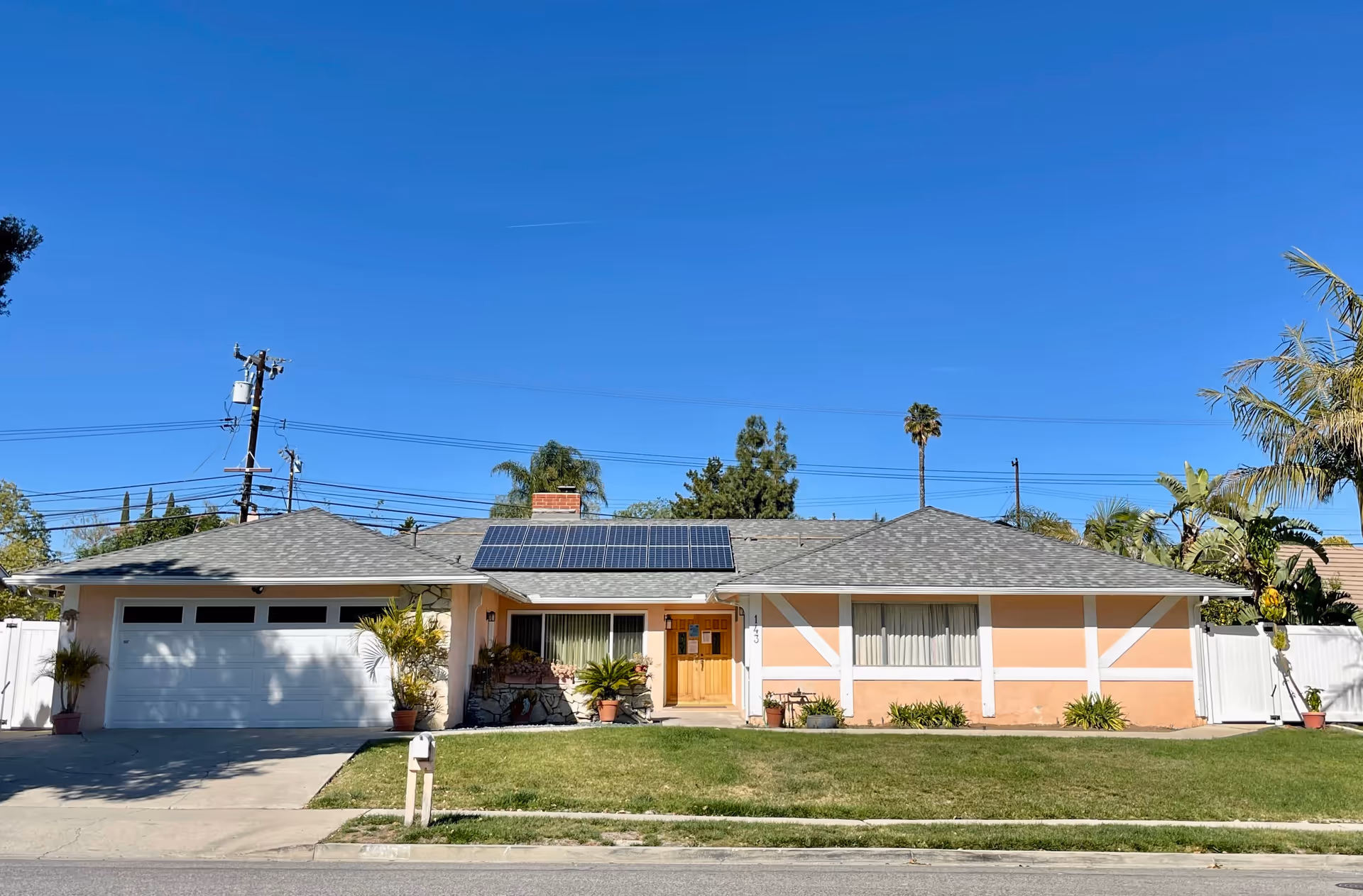 Single-story peach house with white trim, solar panels, and a two-car garage against a blue sky.