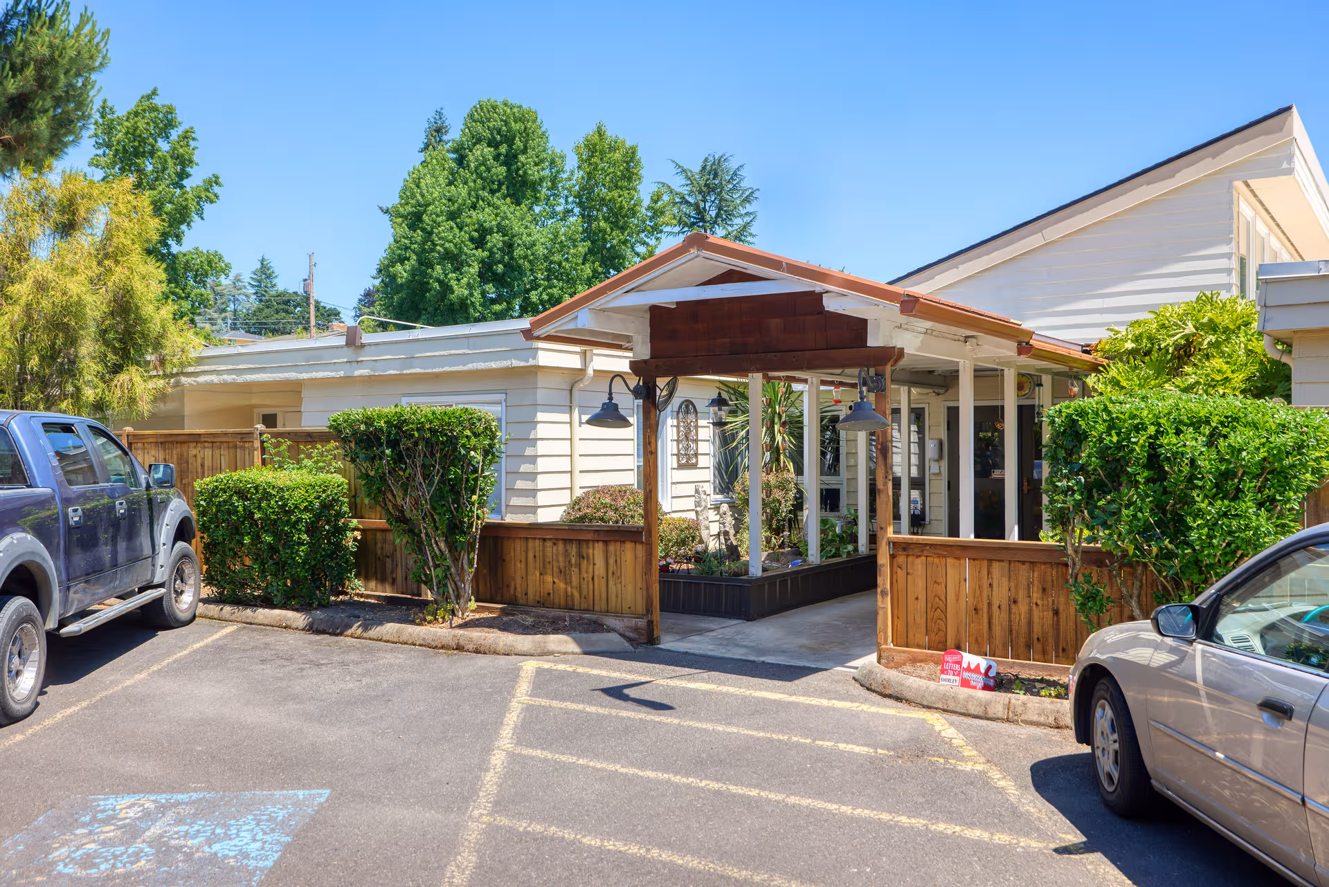 Front view of McKenzie Manor Memory Care building with porch, greenery, and parked cars.