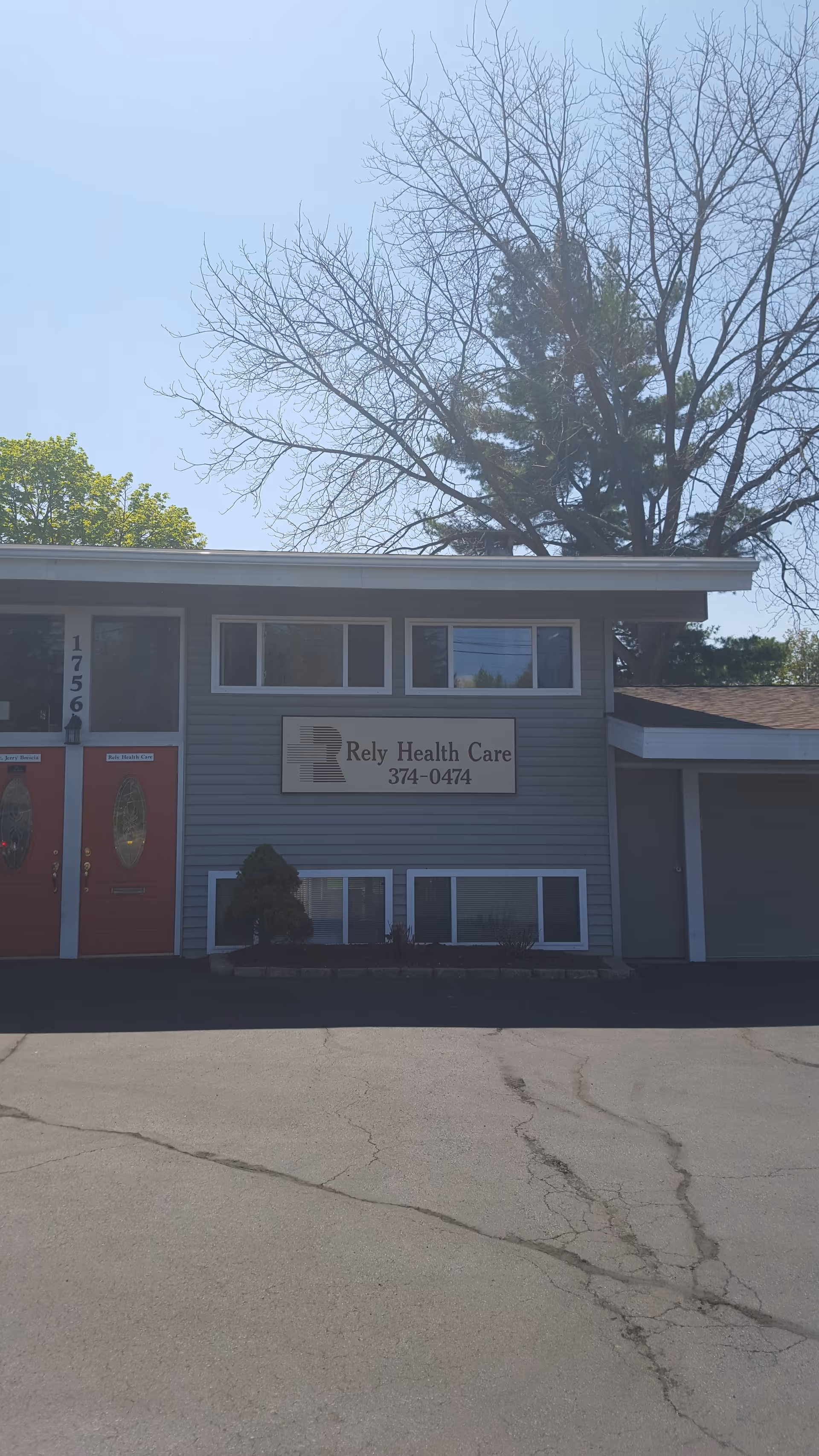 Front view of a two-story care facility exterior with a sign and red entry doors.