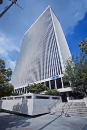 Tall modern glass office building photographed from ground level against a blue sky.