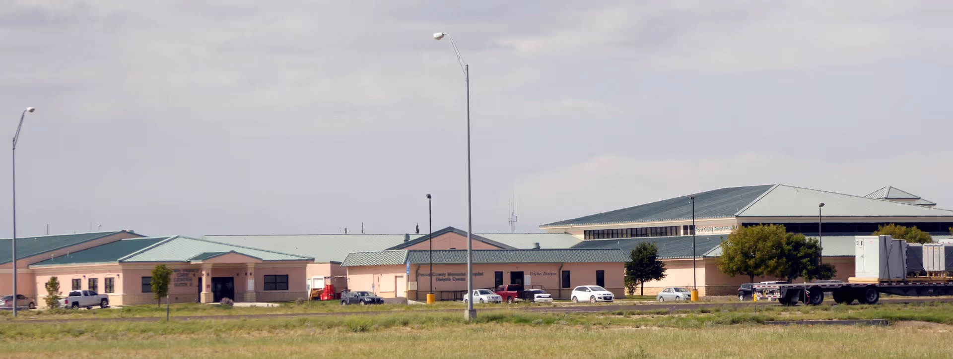 Exterior view of Pecos County Memorial Hospital with green roofs and parked cars.