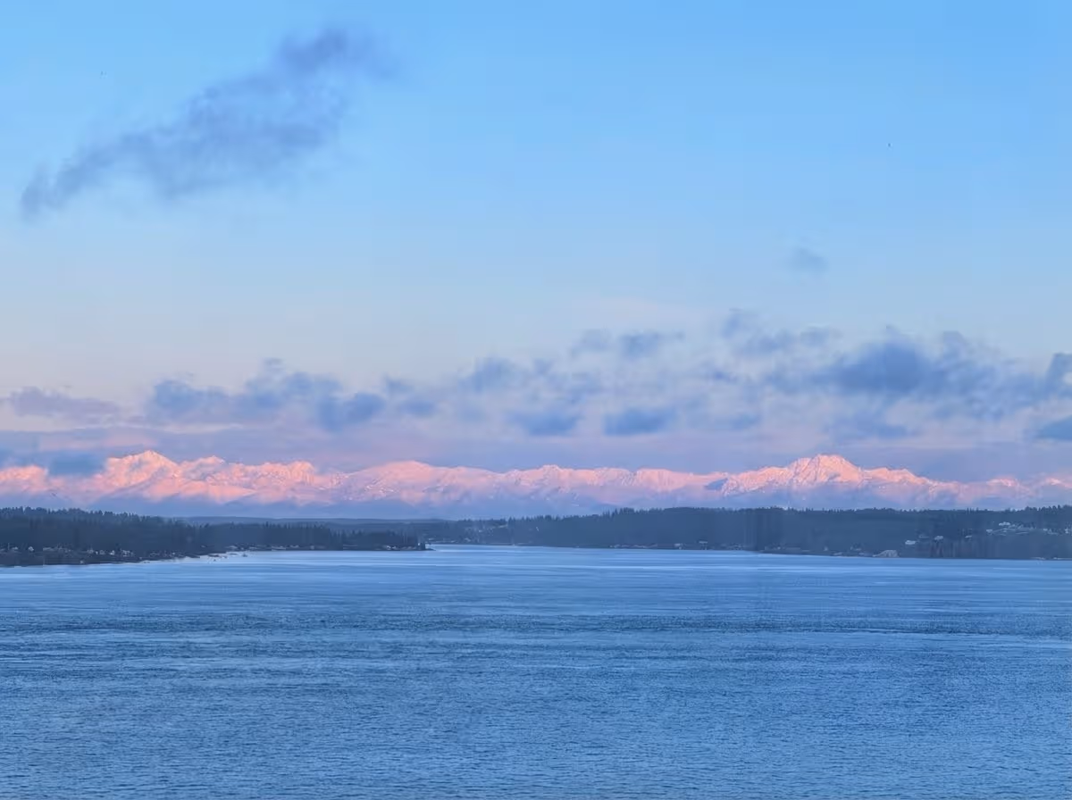 Tranquil waterfront view with snow-capped mountains and pink-tinged sky at dusk.