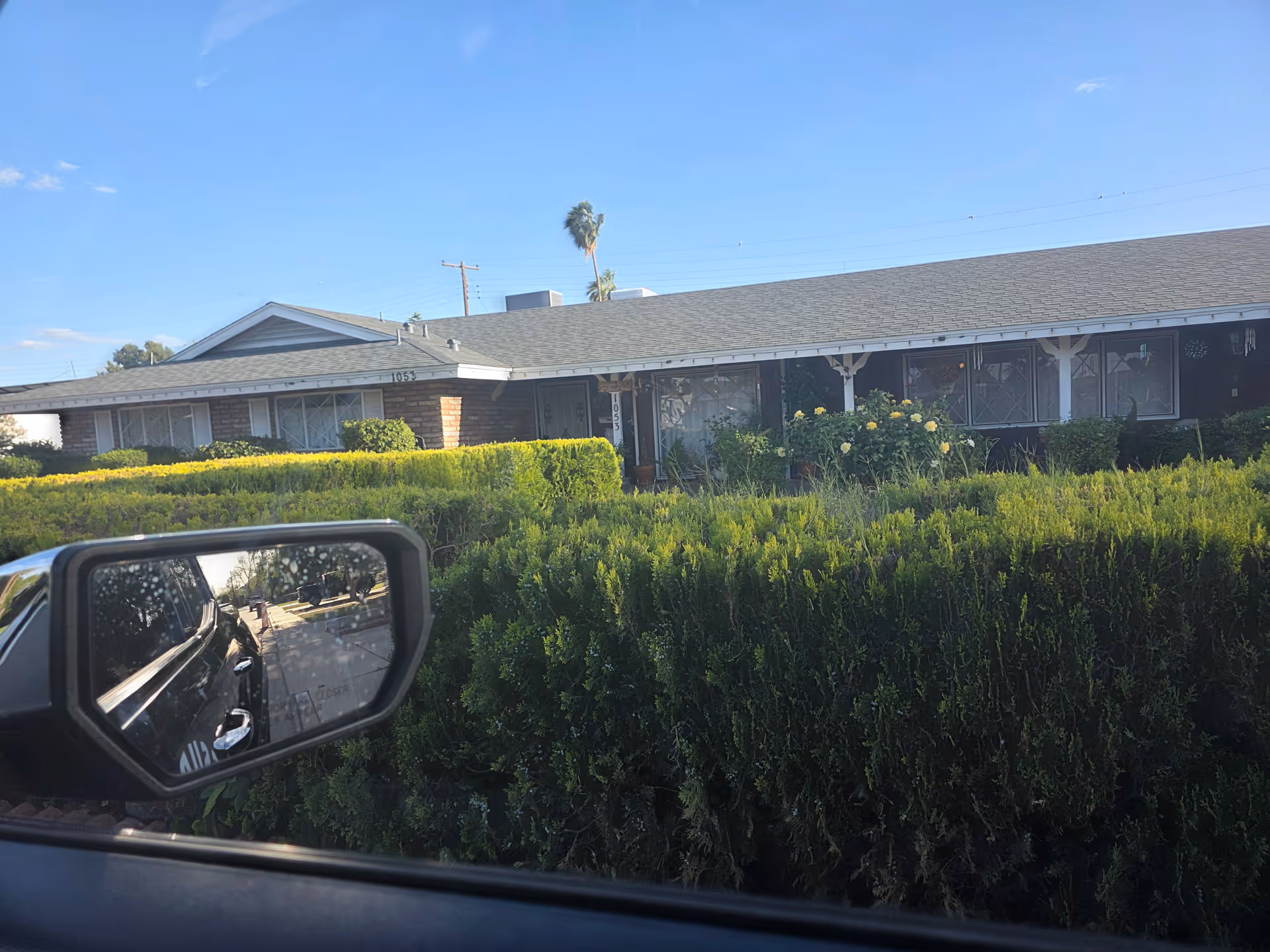 Exterior view of a single-story senior residence with manicured hedges and a car in foreground