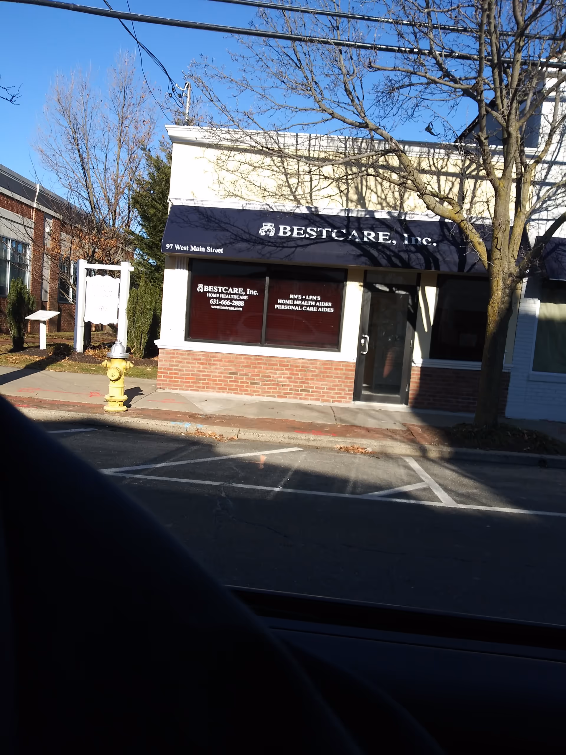 Exterior view of BestCare, Inc. storefront with awning, windows, and a tree-lined street.