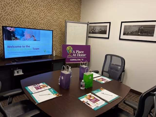 Conference room with a table, brochures, gift bags, TV screen, whiteboard, and wall art.