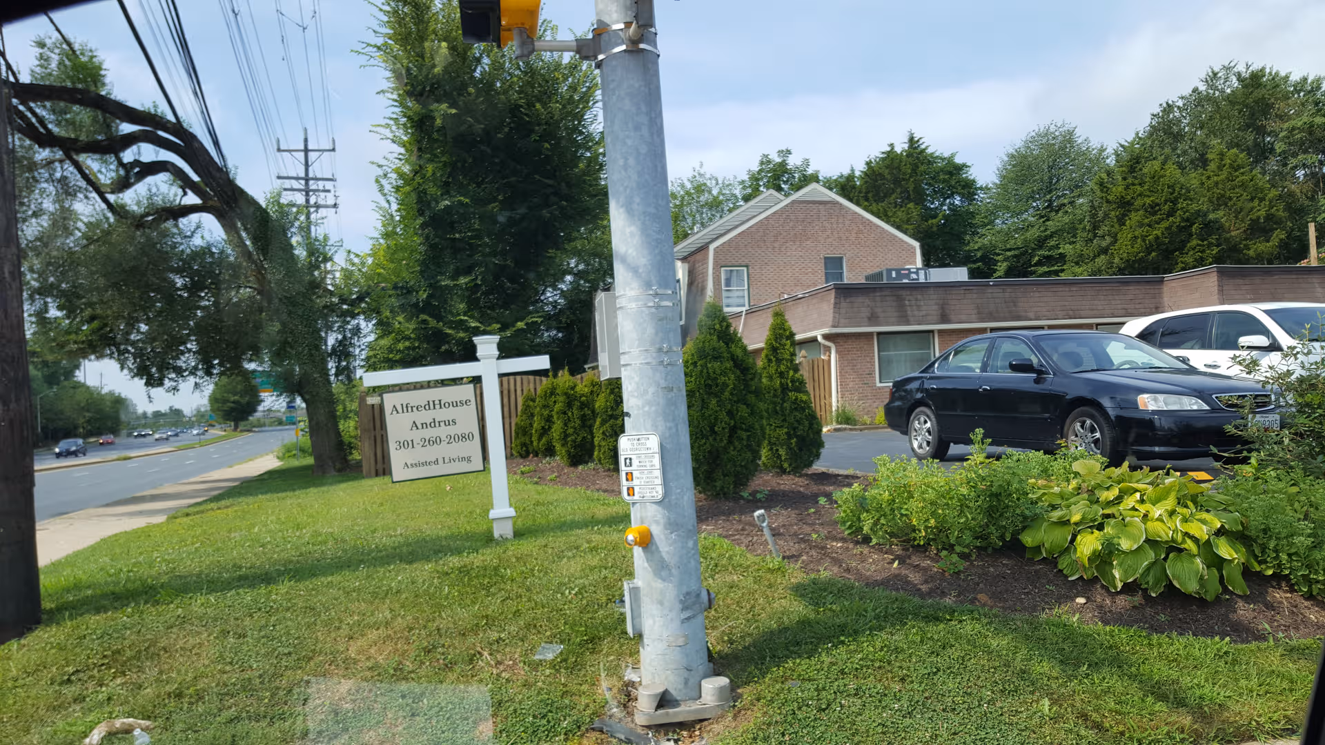 Exterior view of AlfredHouse assisted living with a sign, landscaping, and parked cars.