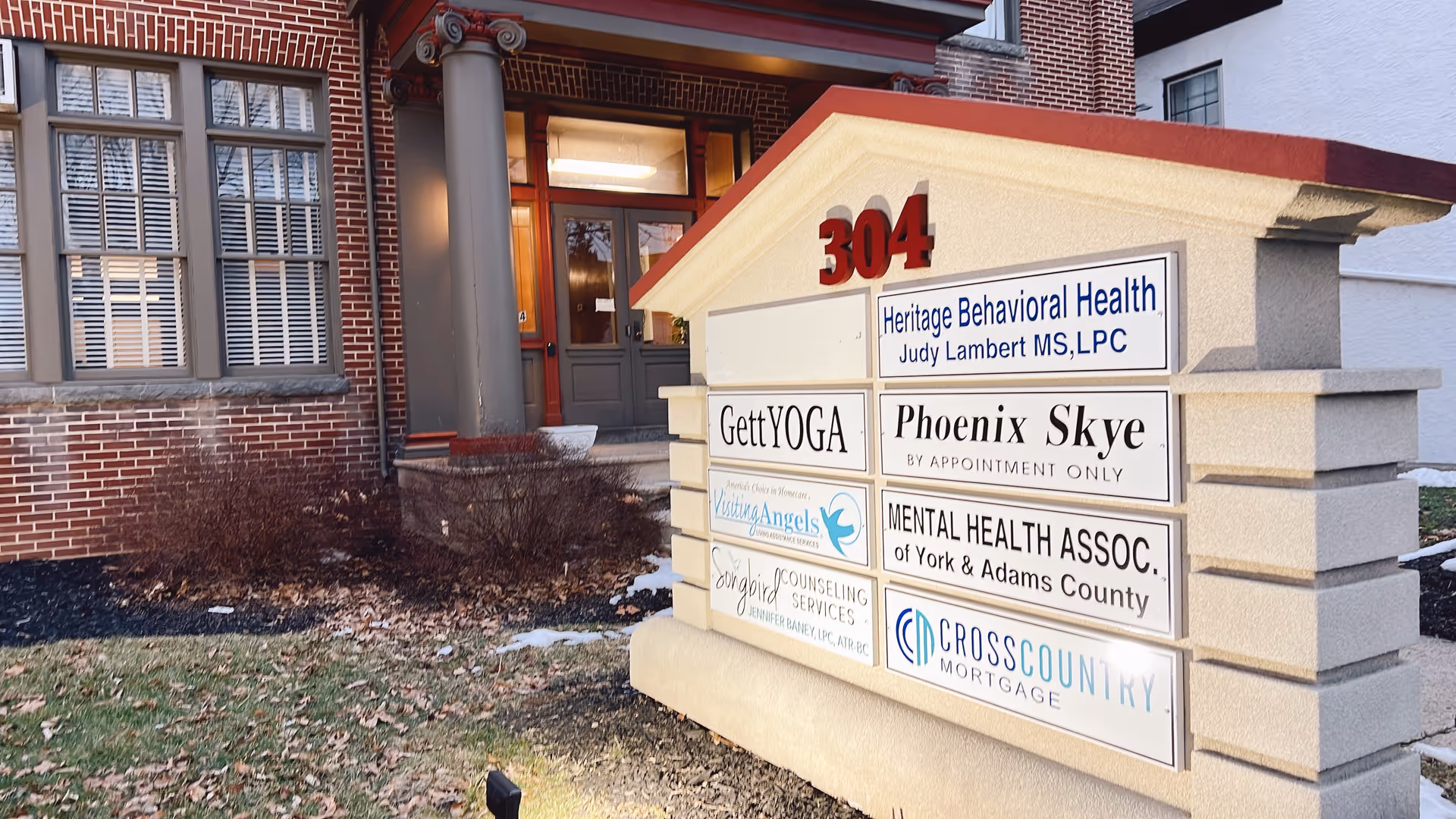 Exterior brick building entrance with stone sign listing multiple business tenants.