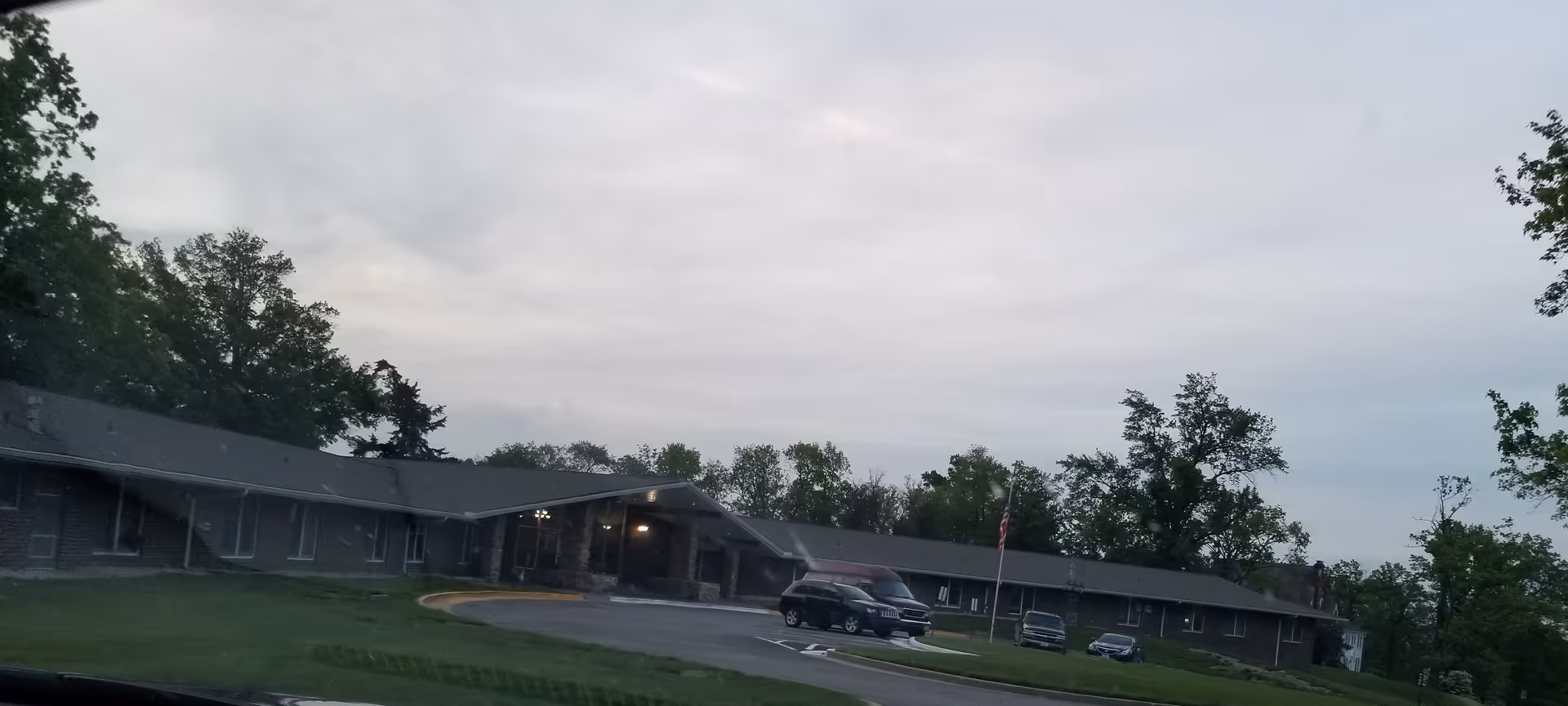 Exterior view of a single-story senior living facility with a curved entrance and parked cars.