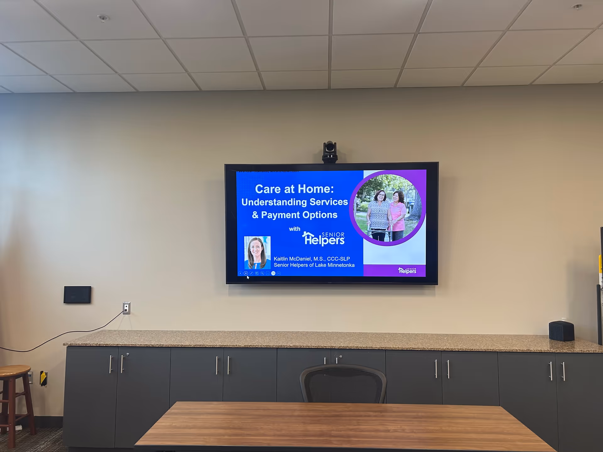 Conference room with wall-mounted presentation screen displaying Care at Home slide.