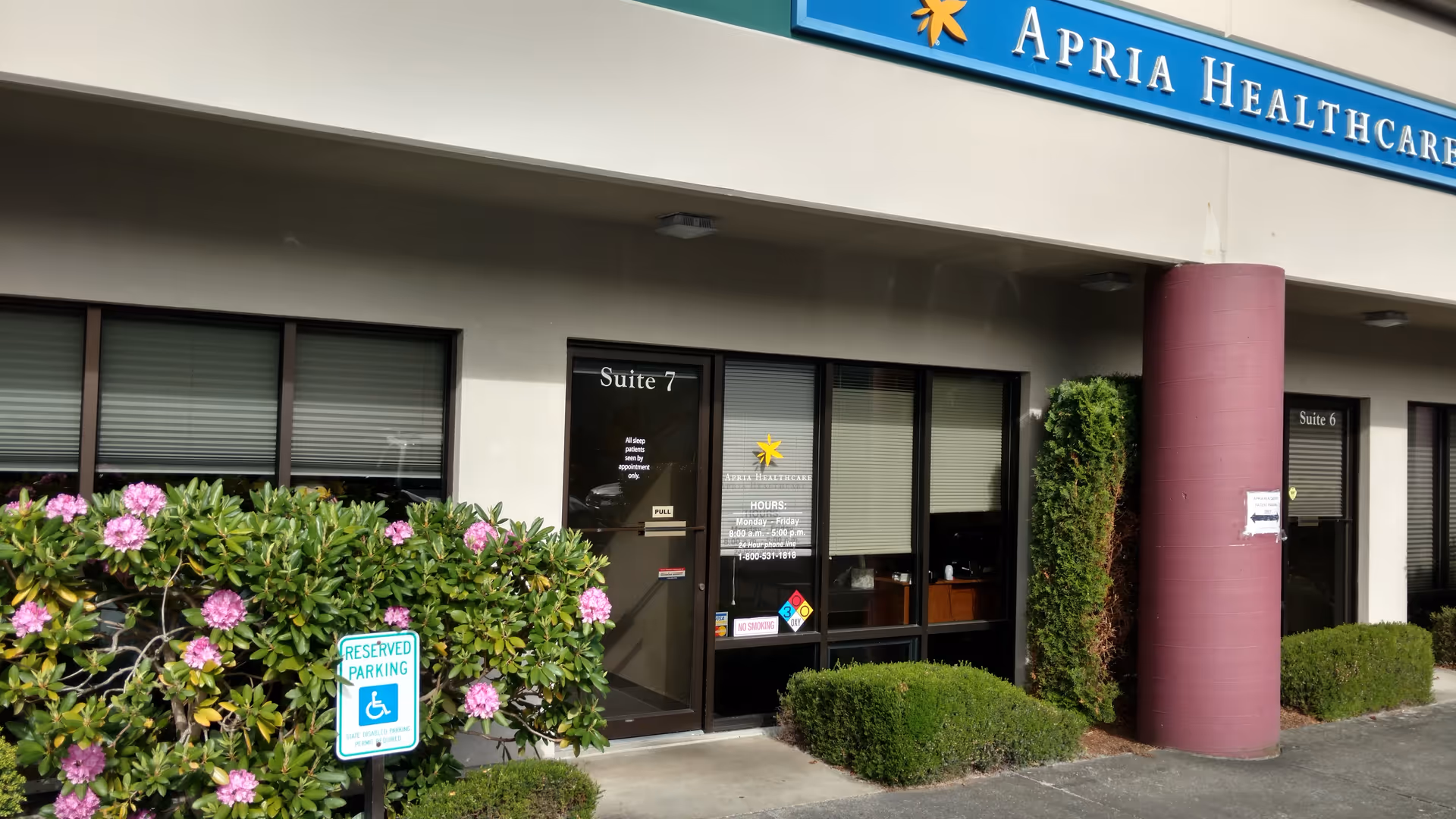 Exterior view of Apria Healthcare facility with glass doors, shrubs, and a reserved parking sign.