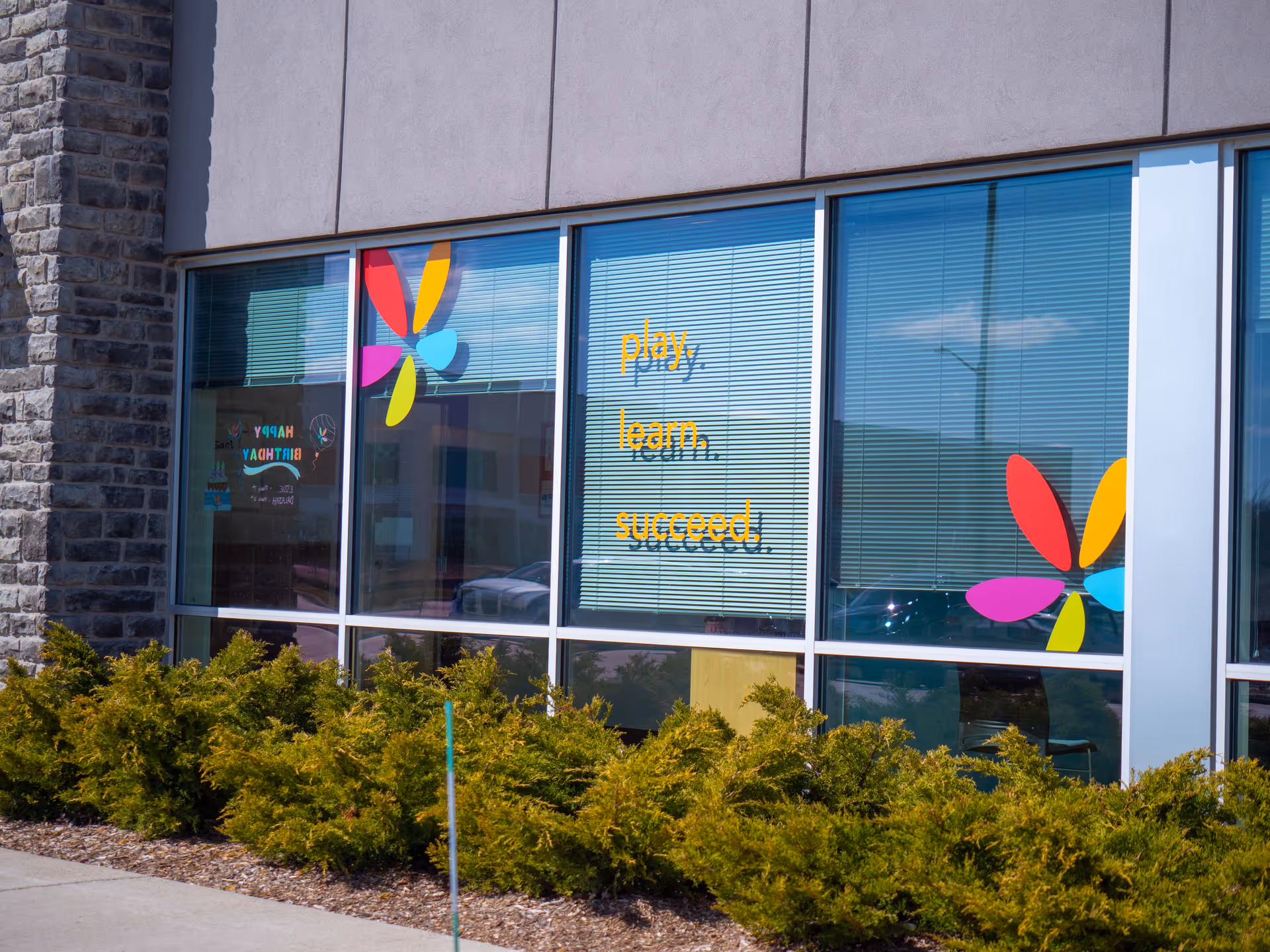 Front of a building with colorful flower-shaped decals on windows and shrubs.