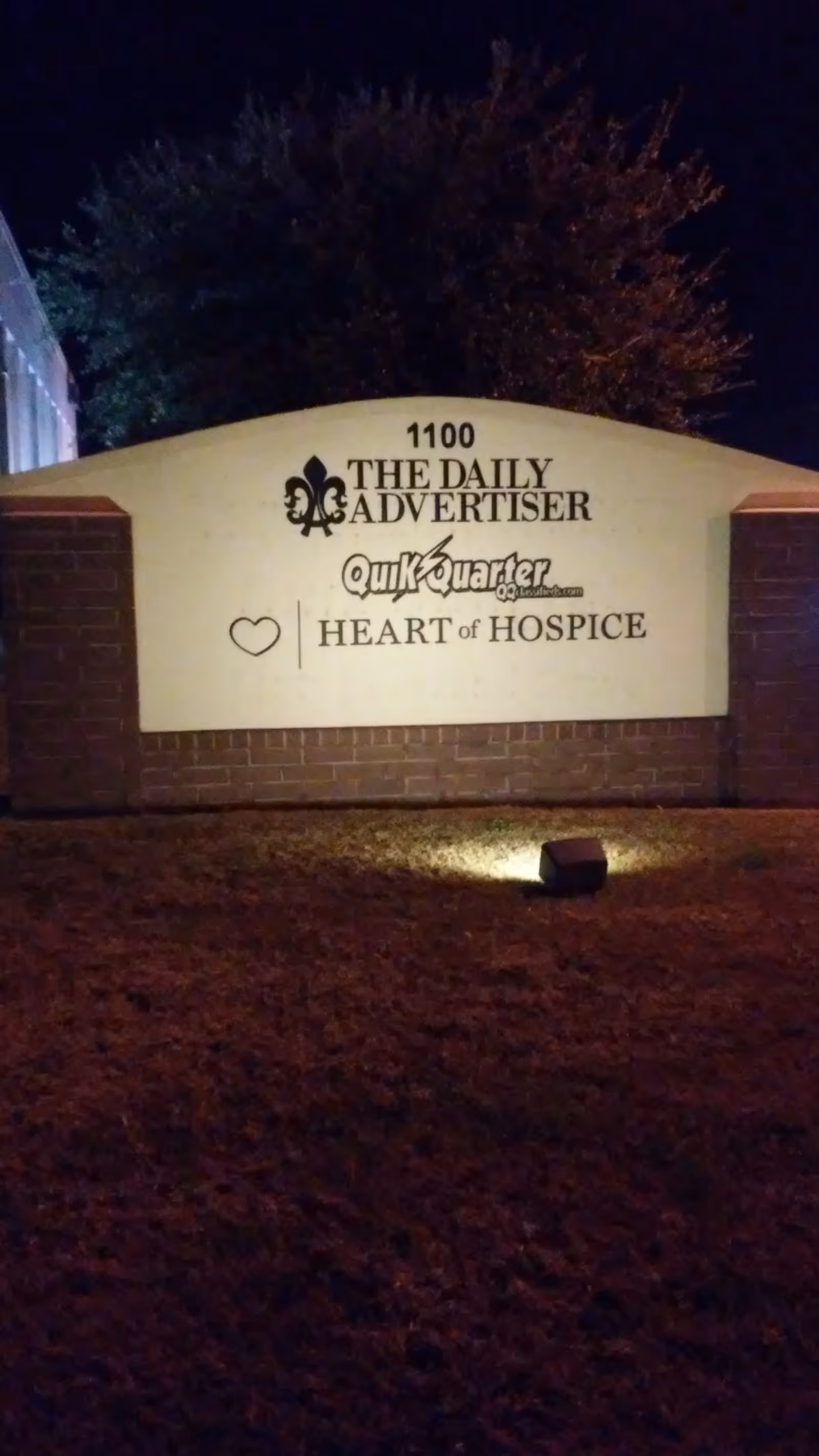Nighttime exterior sign for Heart of Hospice with Daily Advertiser and QuikQuarter logos.