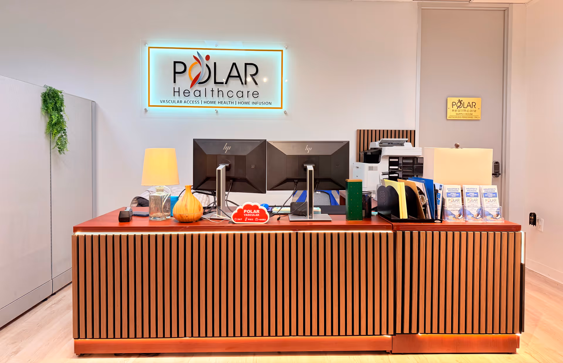 Reception desk with dual monitors, printer, brochures, and a Polar Healthcare sign in a modern lobby.
