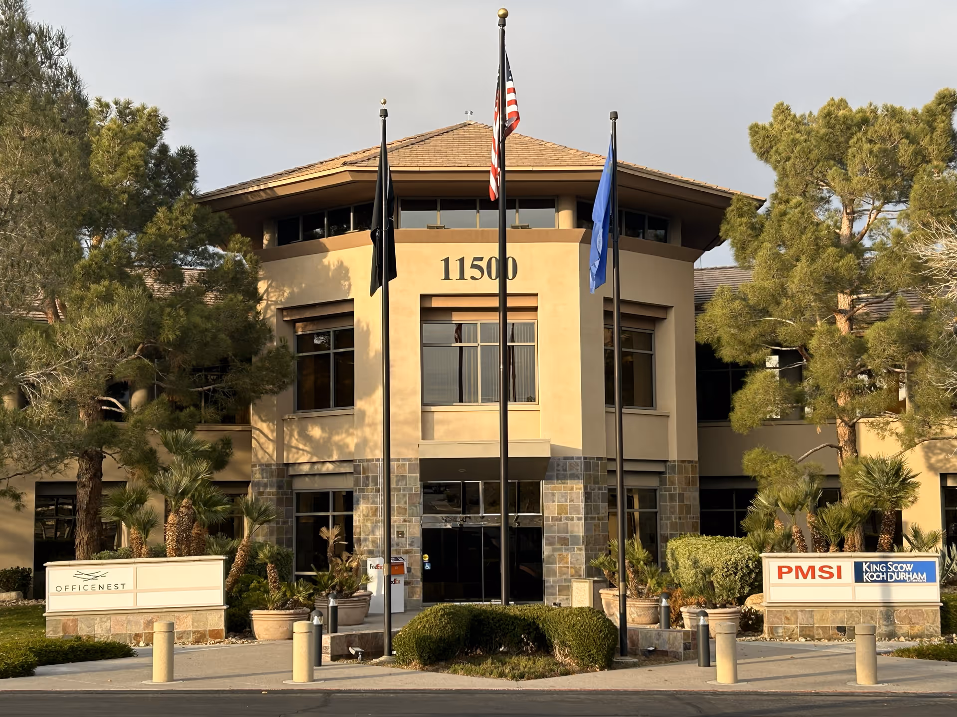 Front view of a beige senior living facility with flags, entrance, and landscaping.