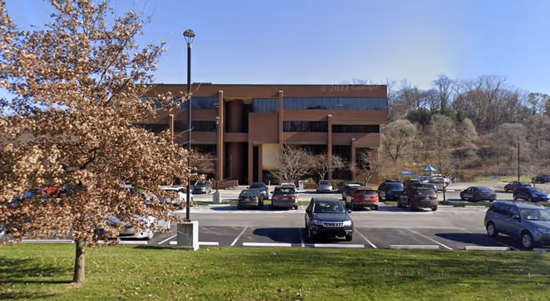Brick building with a parking lot and surrounding leafless trees in front.
