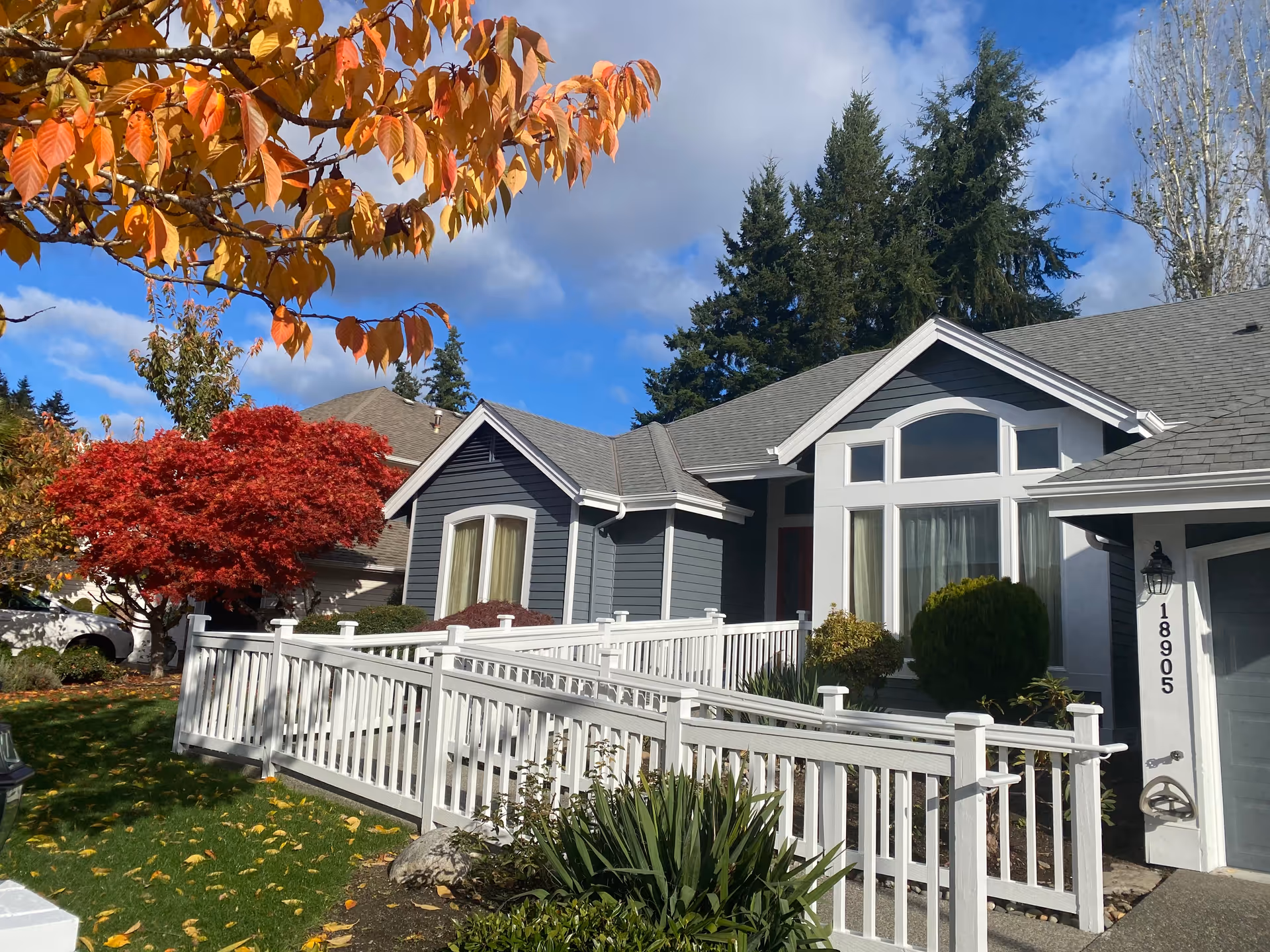 Harmony Place Adult Family Home exterior: blue-gray house with white fence and autumn trees.