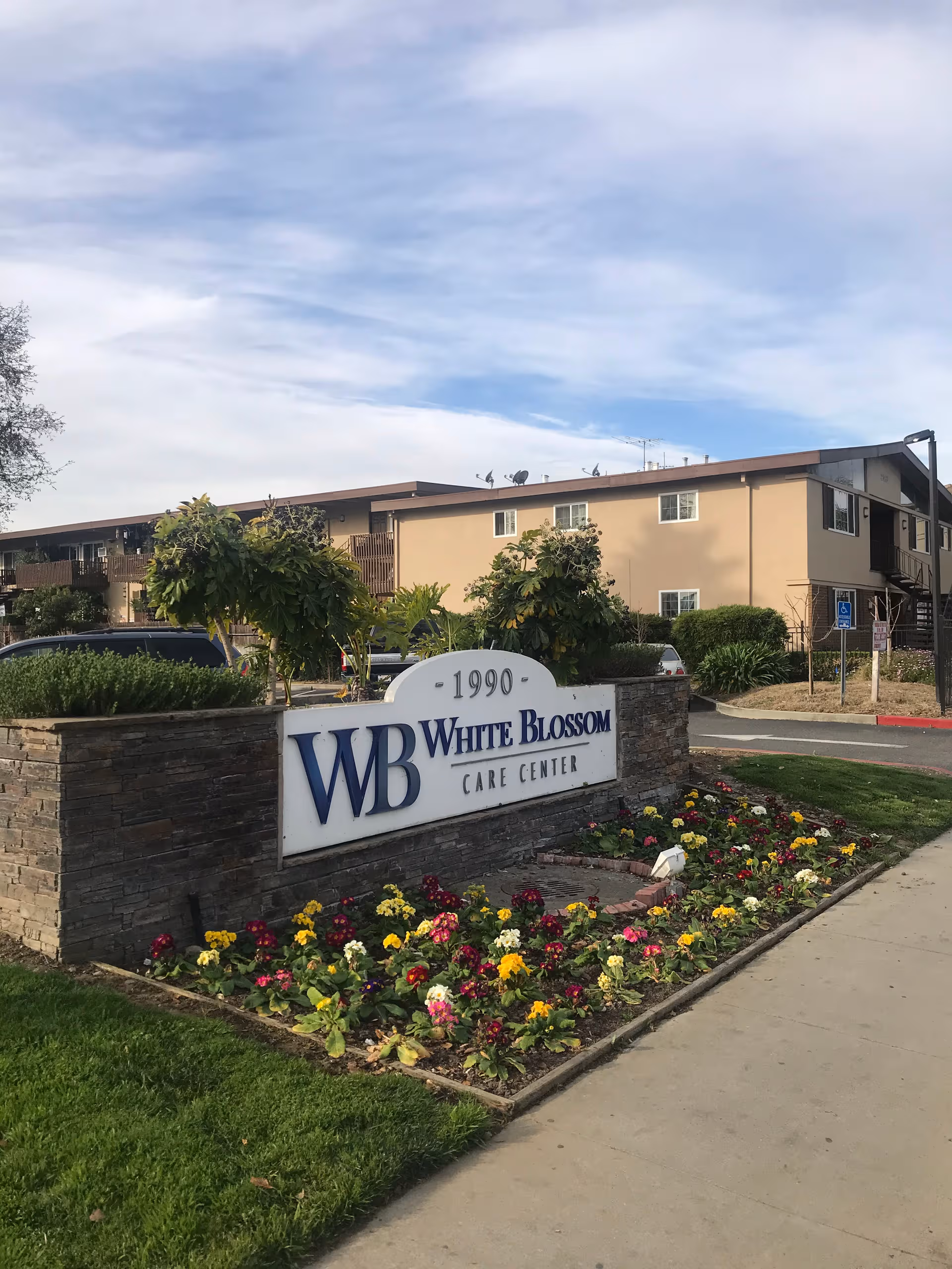 Exterior view of White Blossom Care Center sign with flowers and beige building backdrop