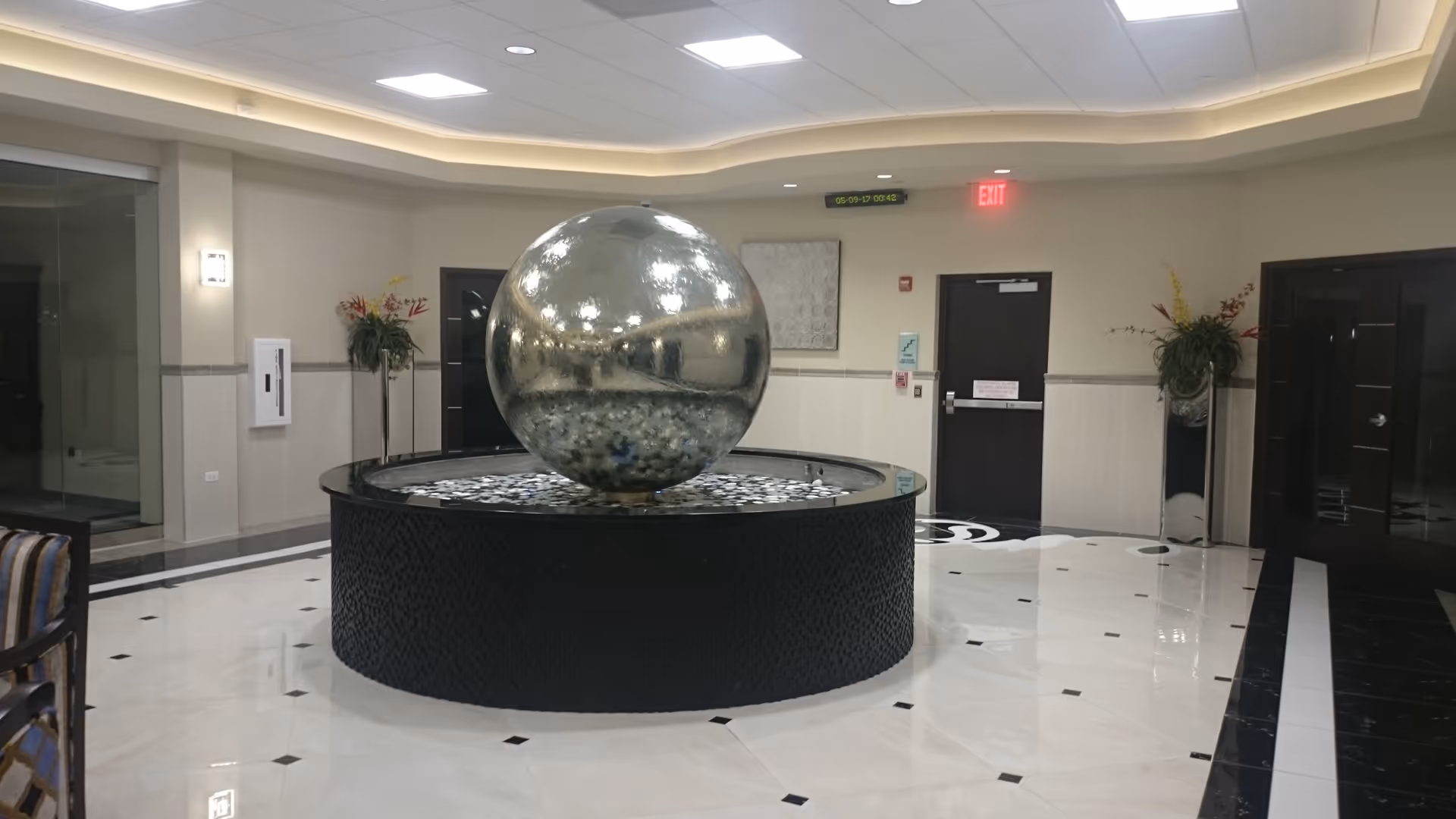 A modern lobby features a round reflective fountain centerpiece and marble floor.
