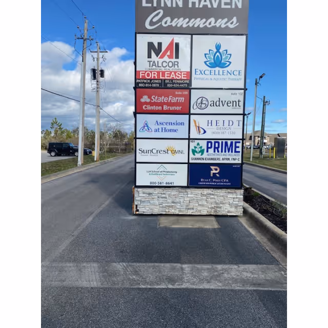 Tall outdoor signboard with multiple business logos beside a road.