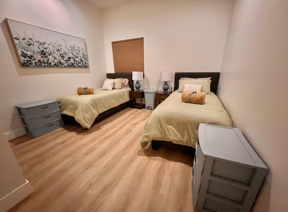 Two twin beds with beige bedding and matching nightstands in a small bedroom.